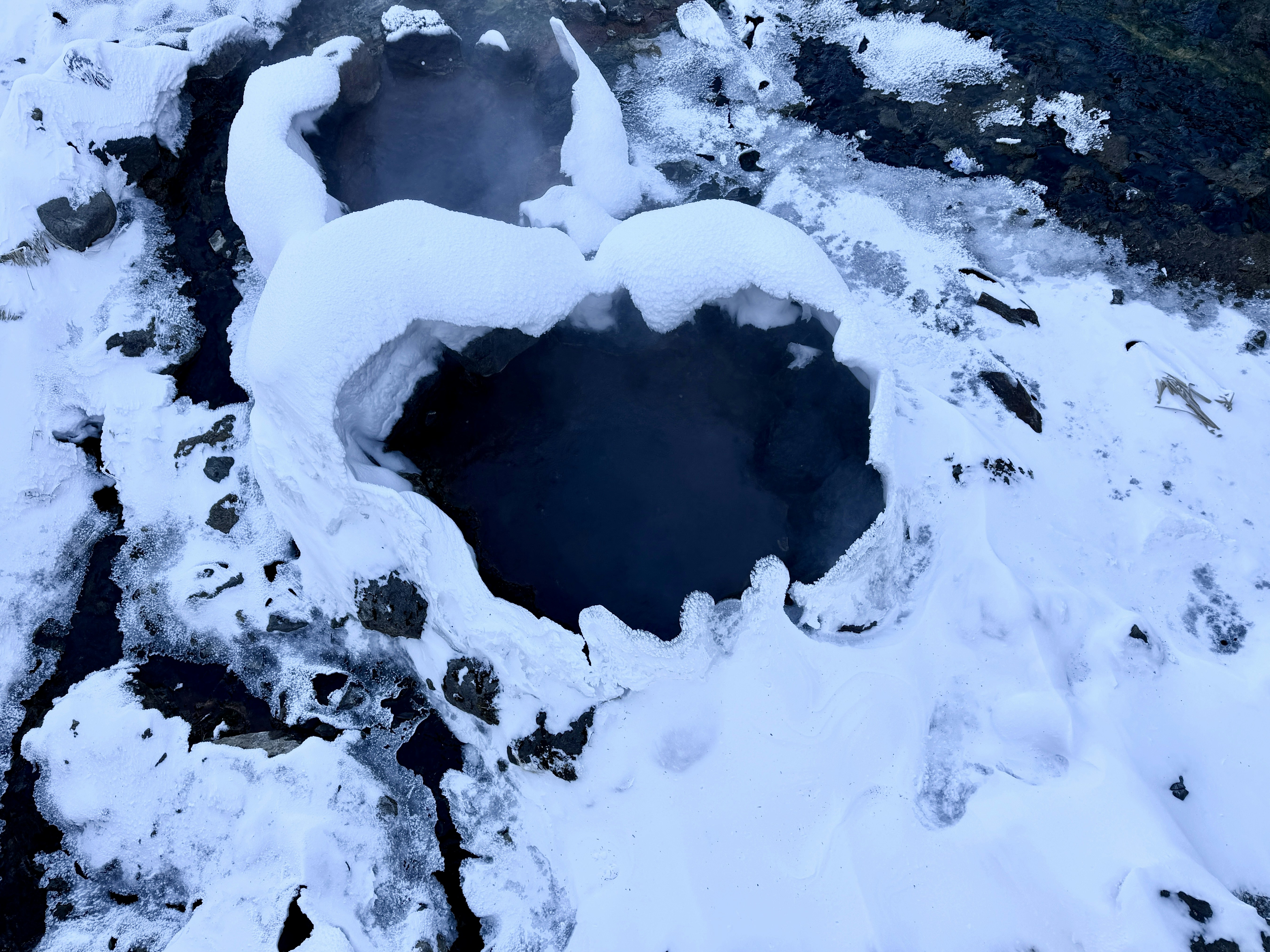 A steaming hot spring surrounded by snow and ice.