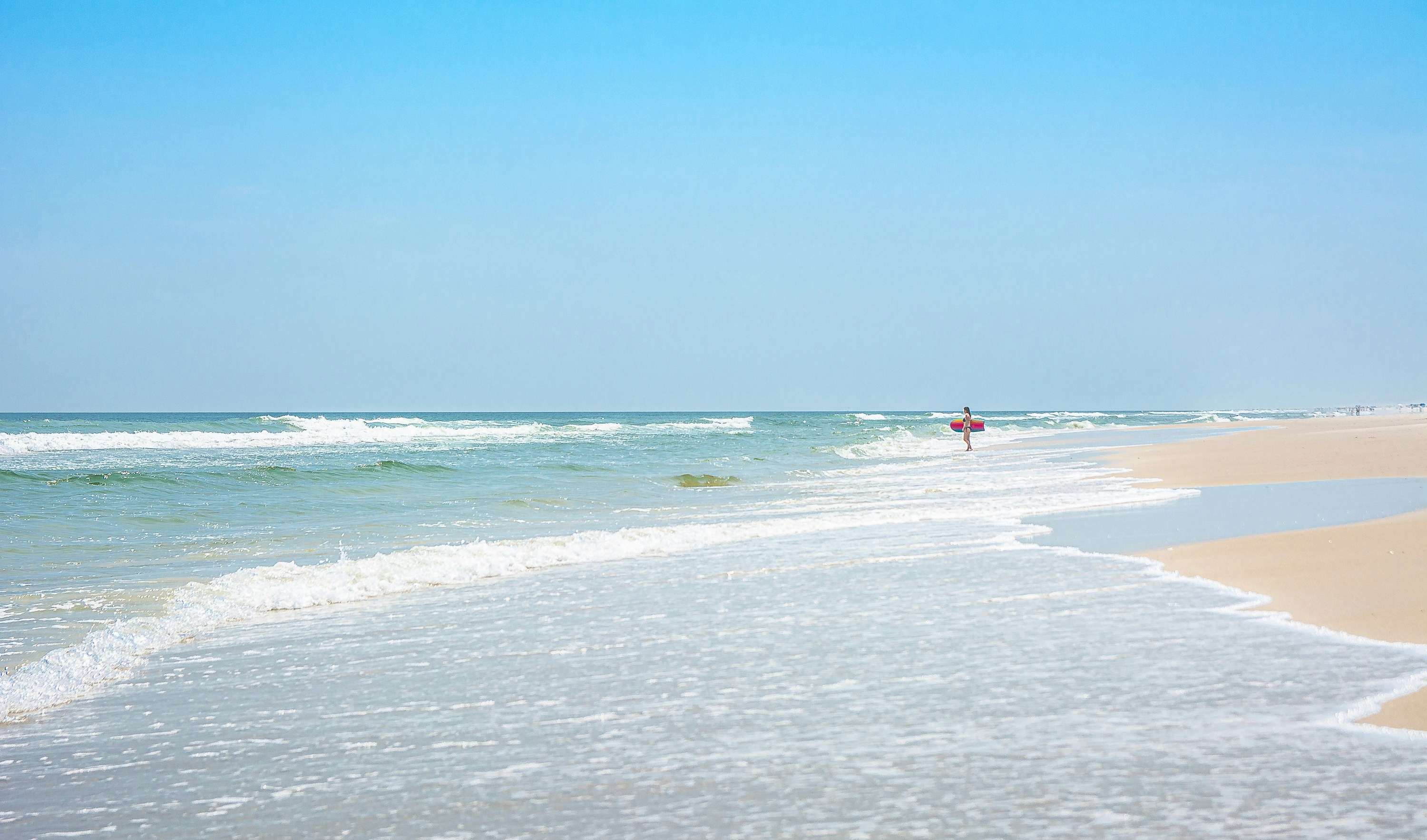 A person walks along a sandy beach with gentle waves.