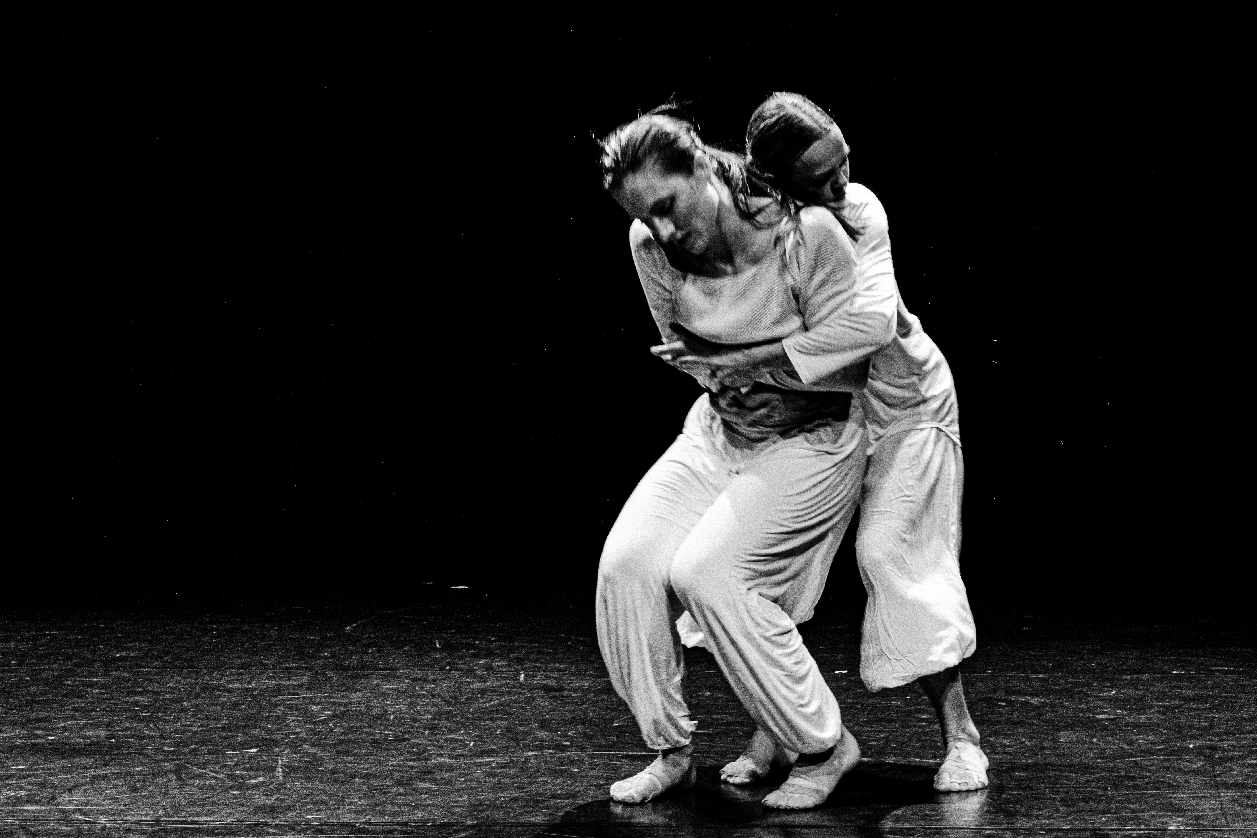 Two dancers in white outfits embrace on stage.