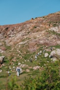 A group of hikers ascend a rocky, grassy hill.