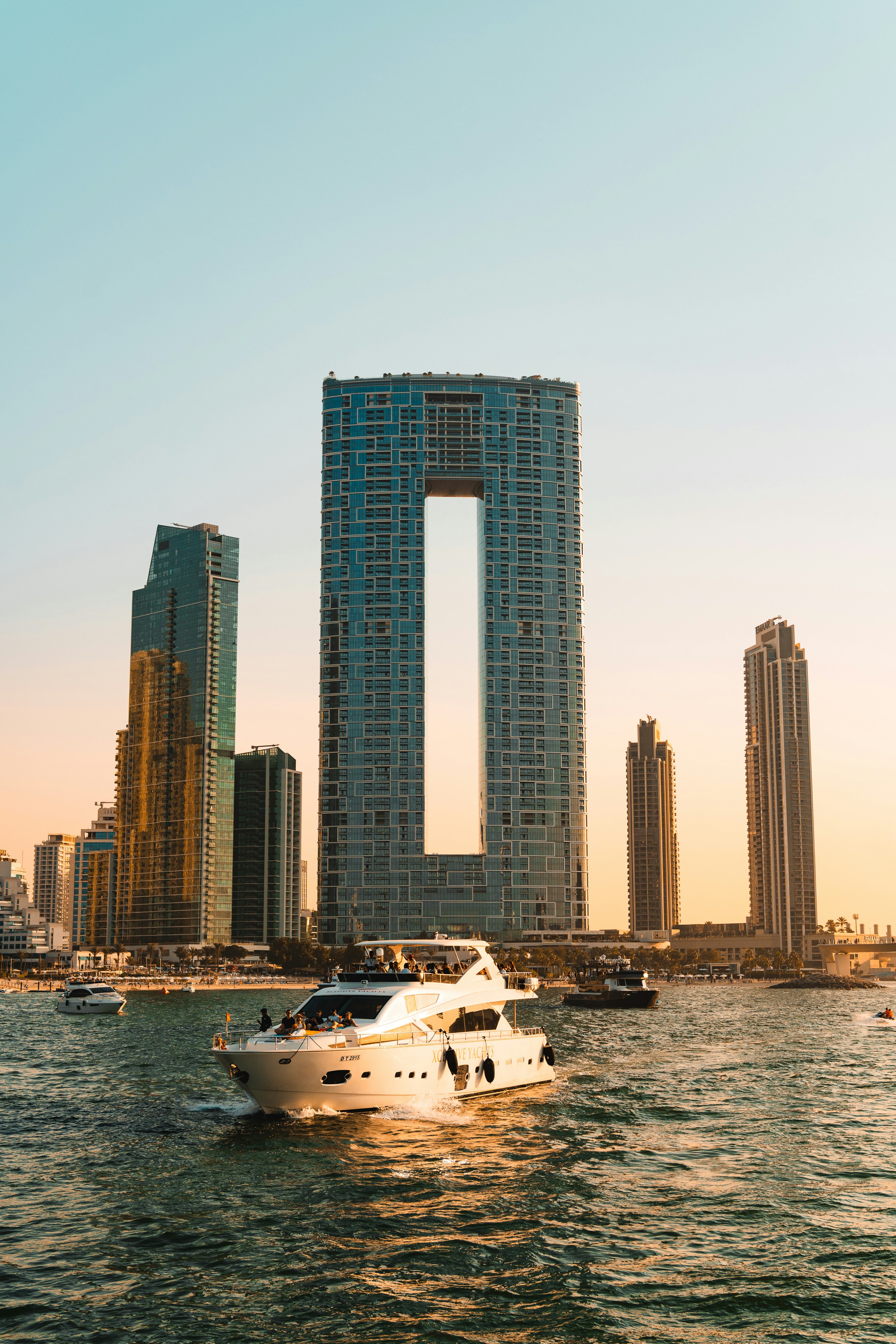 Yacht sailing past modern skyscrapers at sunset