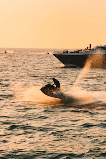 Person riding jet ski with boat in background at sunset