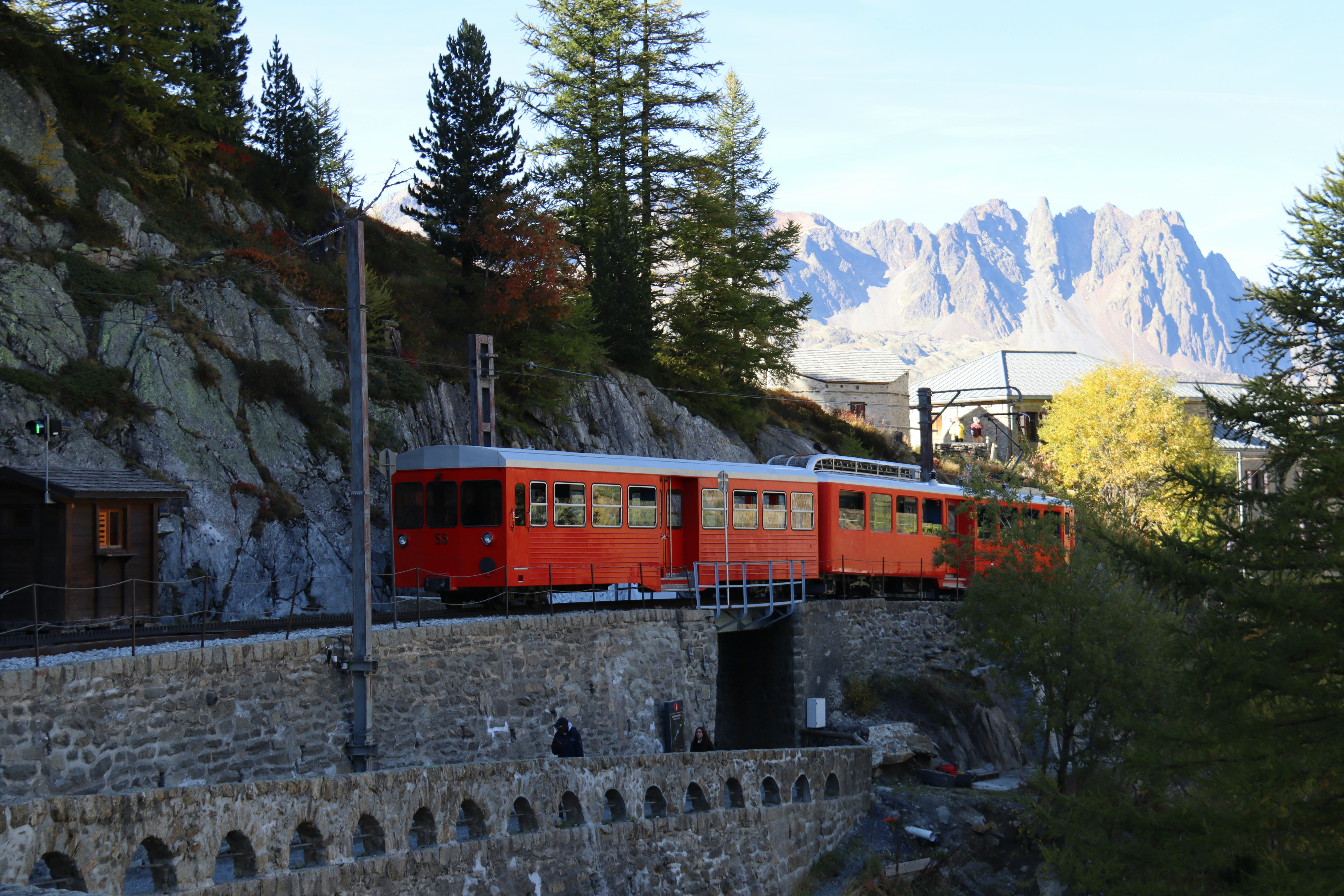 Red train travels on a scenic mountain railway.