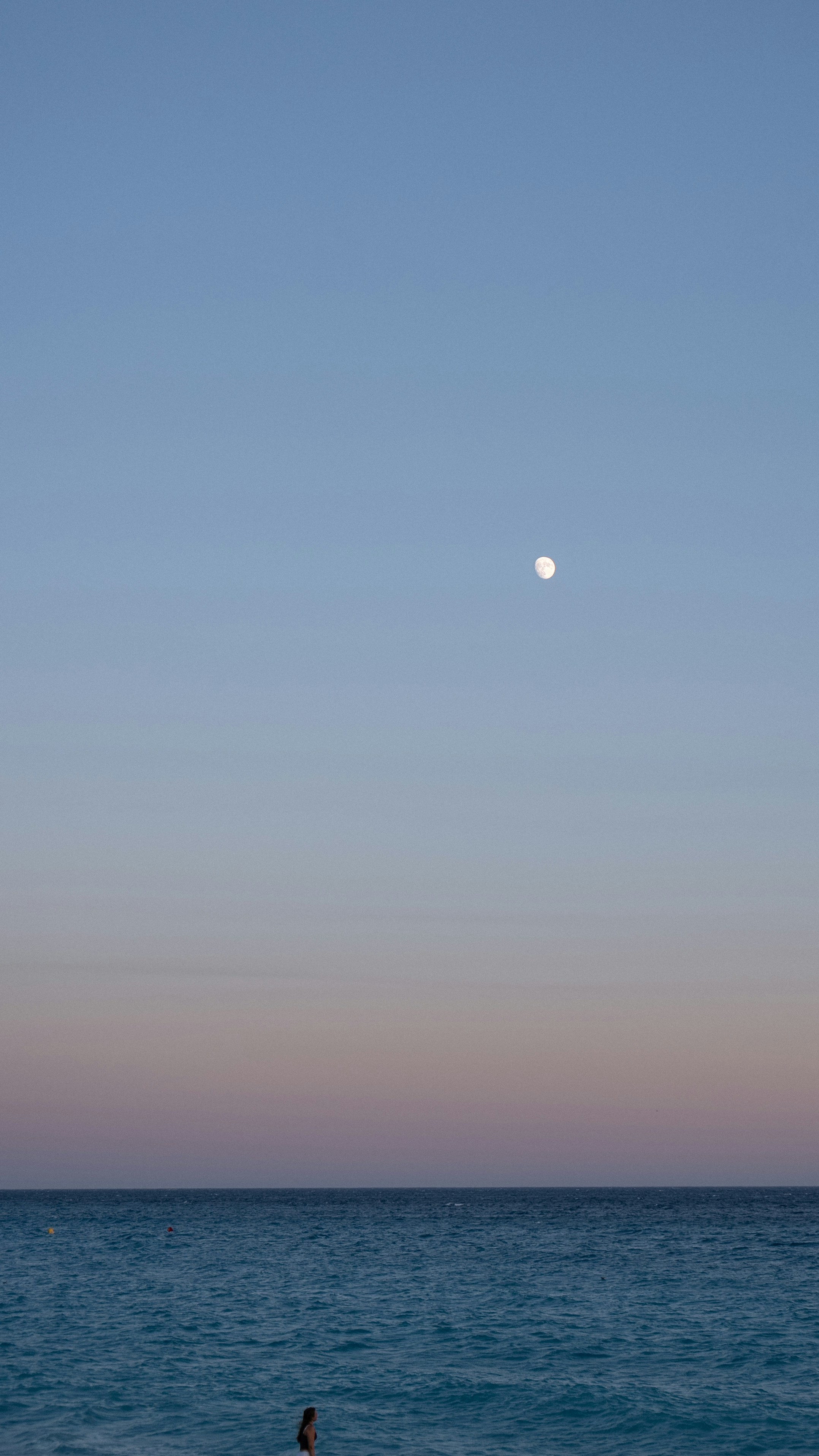 A person standing in the ocean under a full moon.