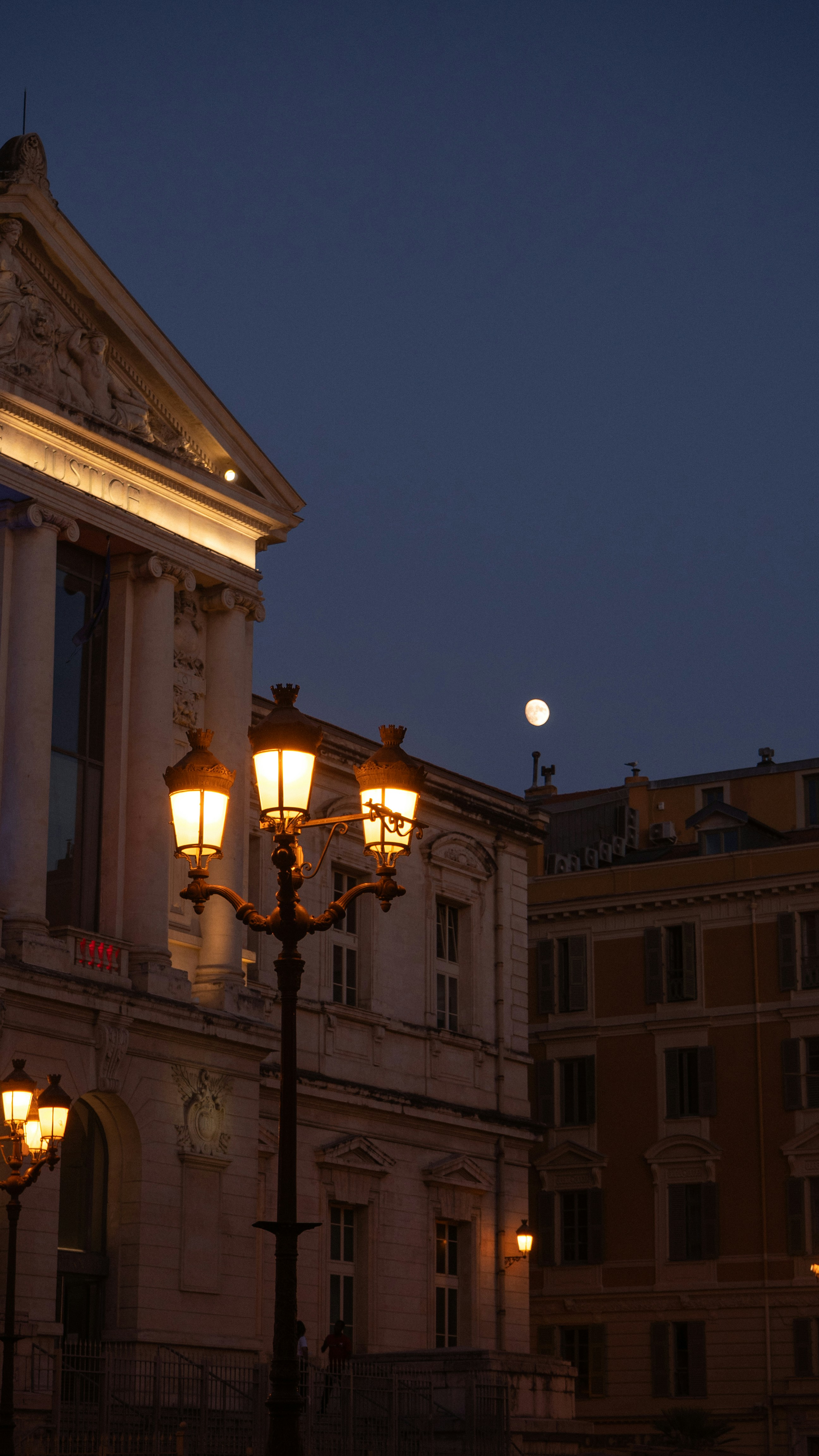 Street lamps illuminate buildings under a twilight sky with moon.