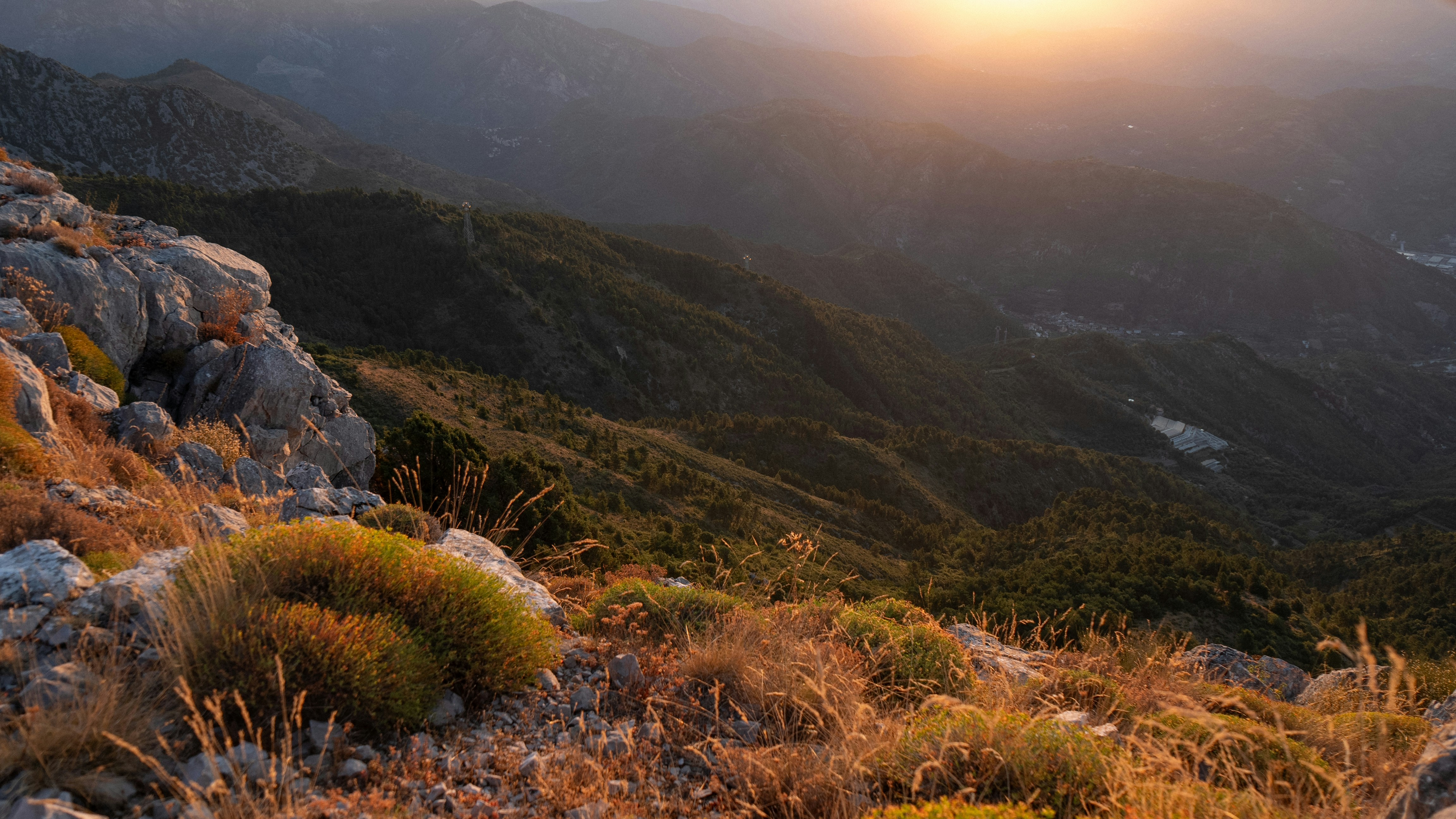 Golden sunset over rolling green mountains and rocky foreground