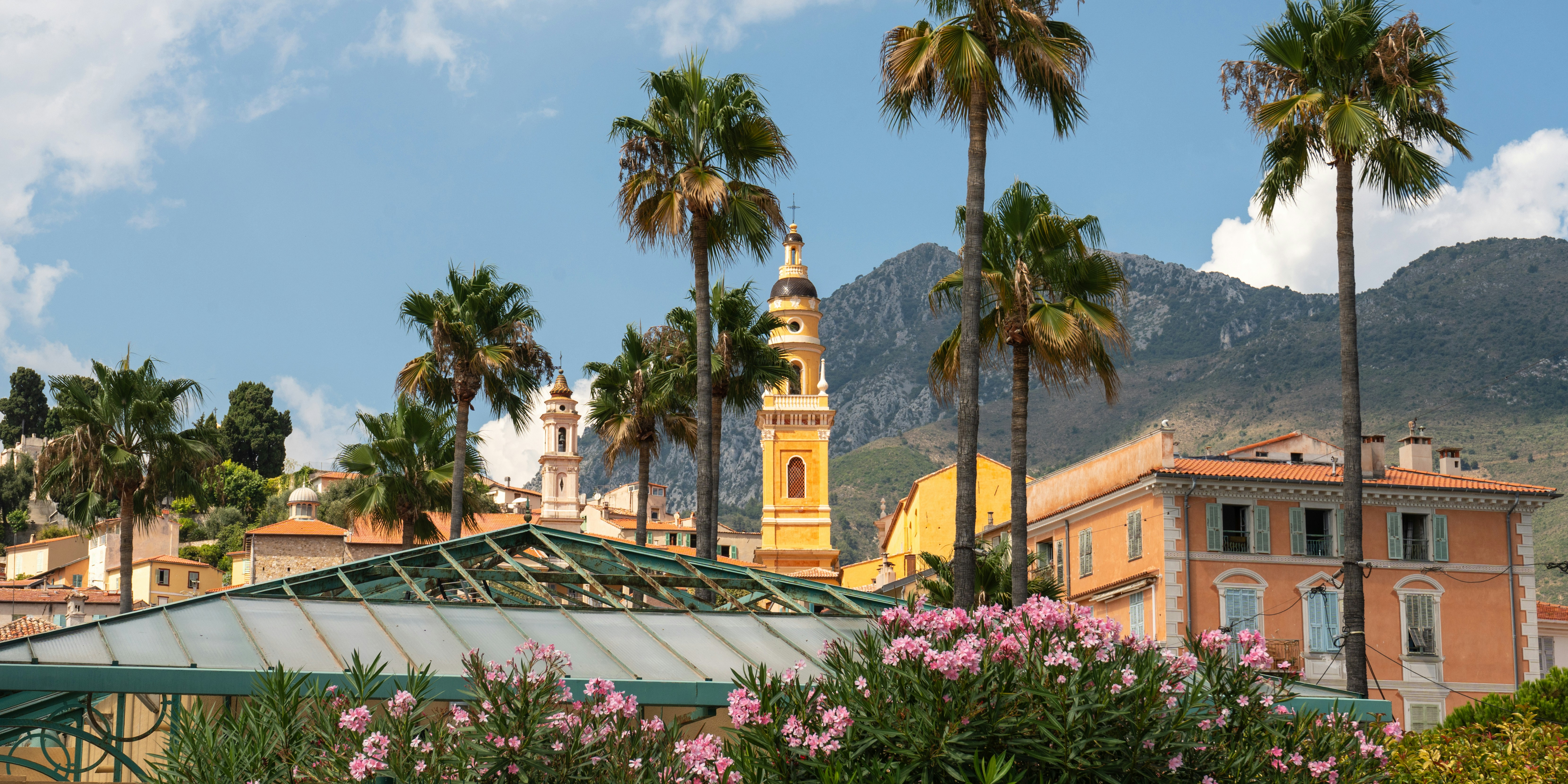 Palm trees overlook buildings and mountains under a blue sky.