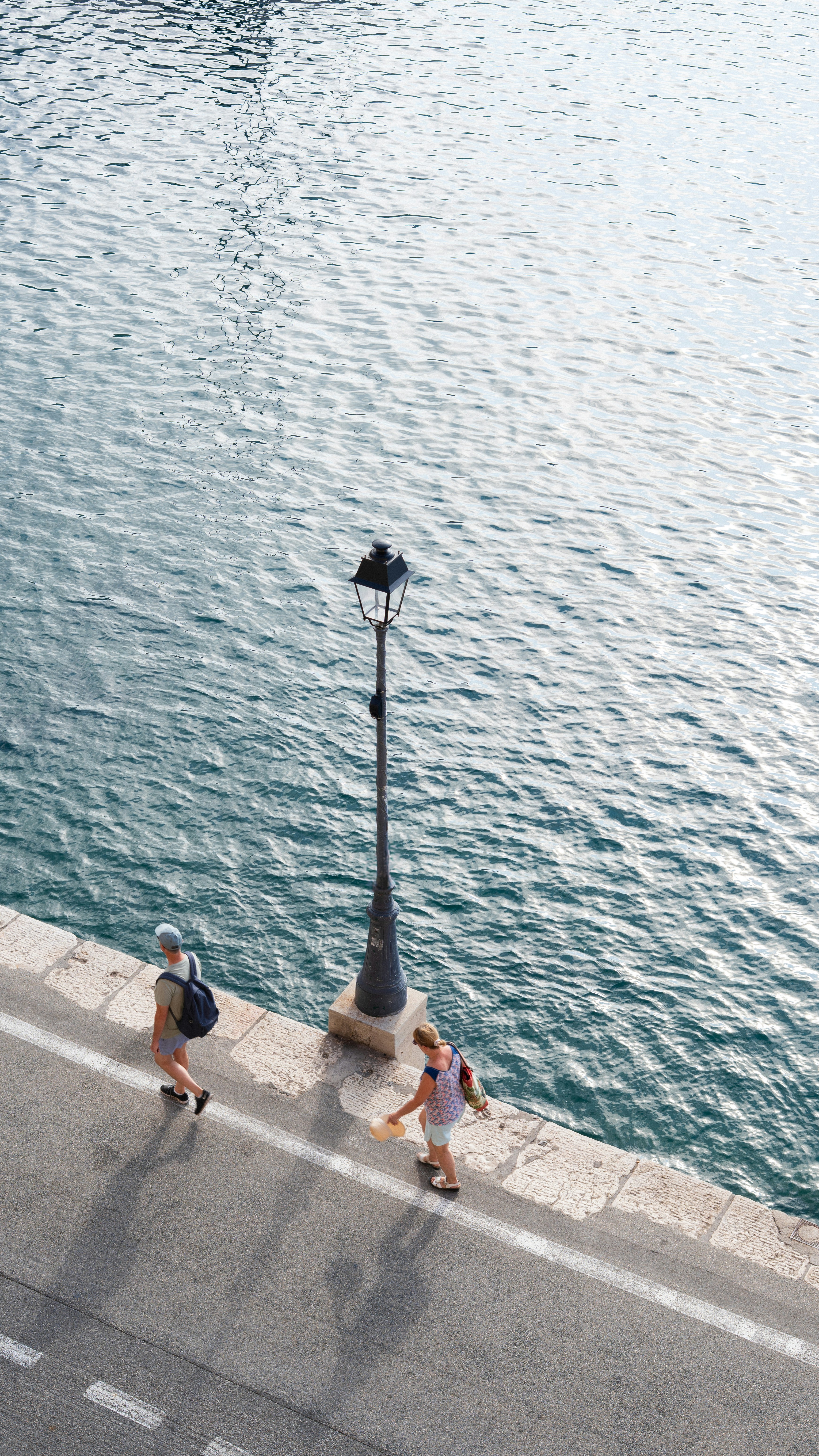 Two people walk along a waterfront beside a lamppost.
