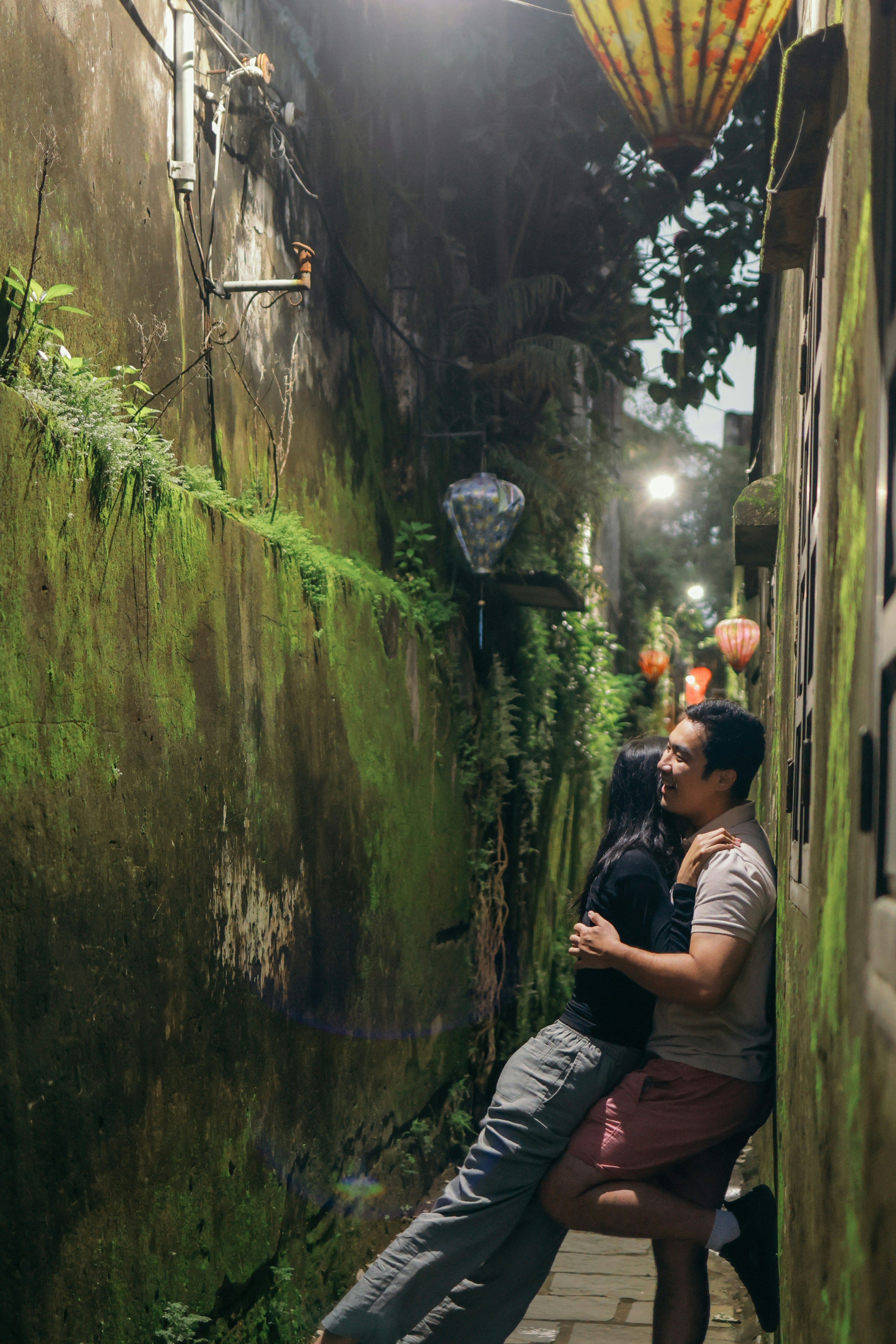 Couple embracing in a narrow, moss-covered alley at night.