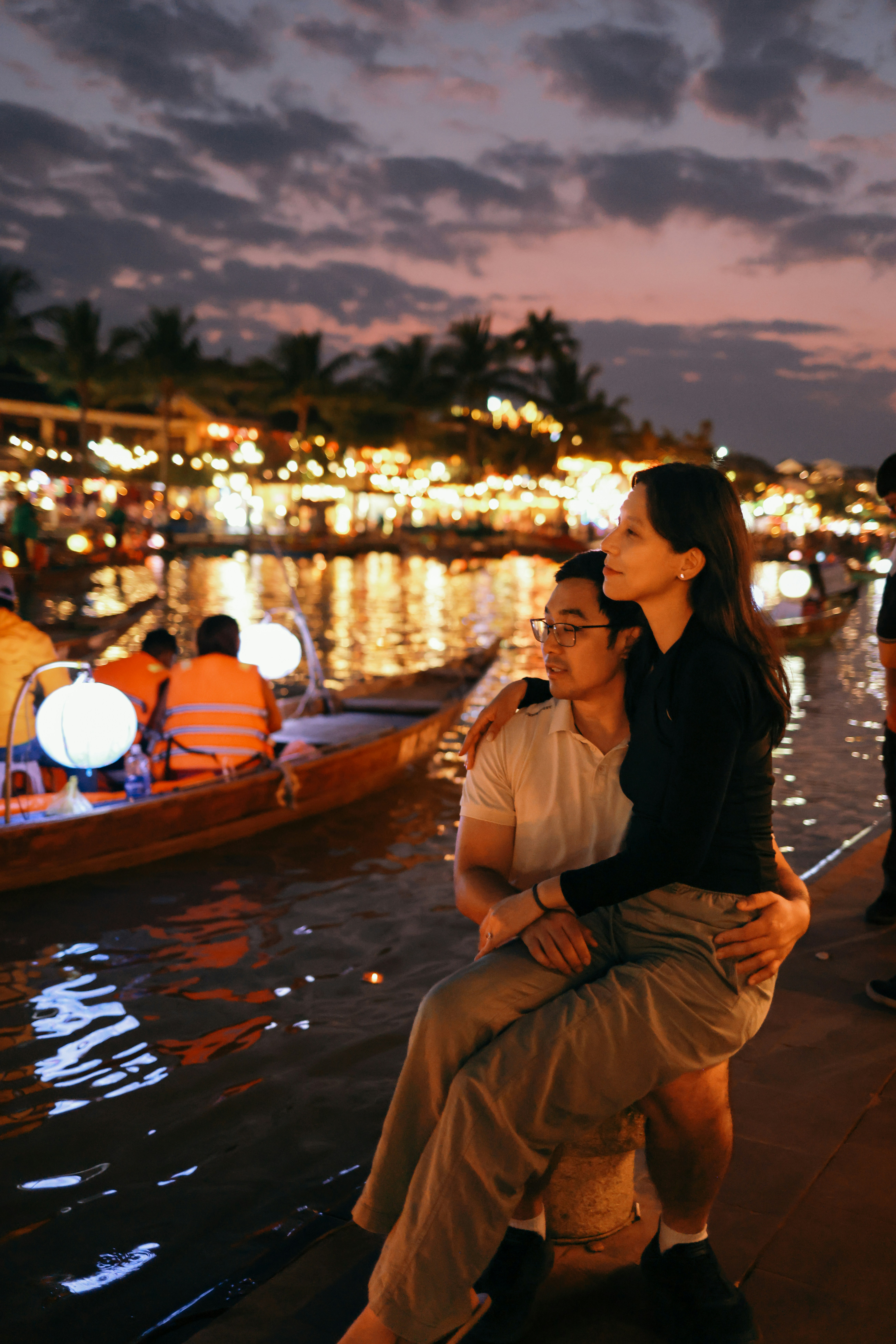 Couple sitting by a river at dusk with city lights