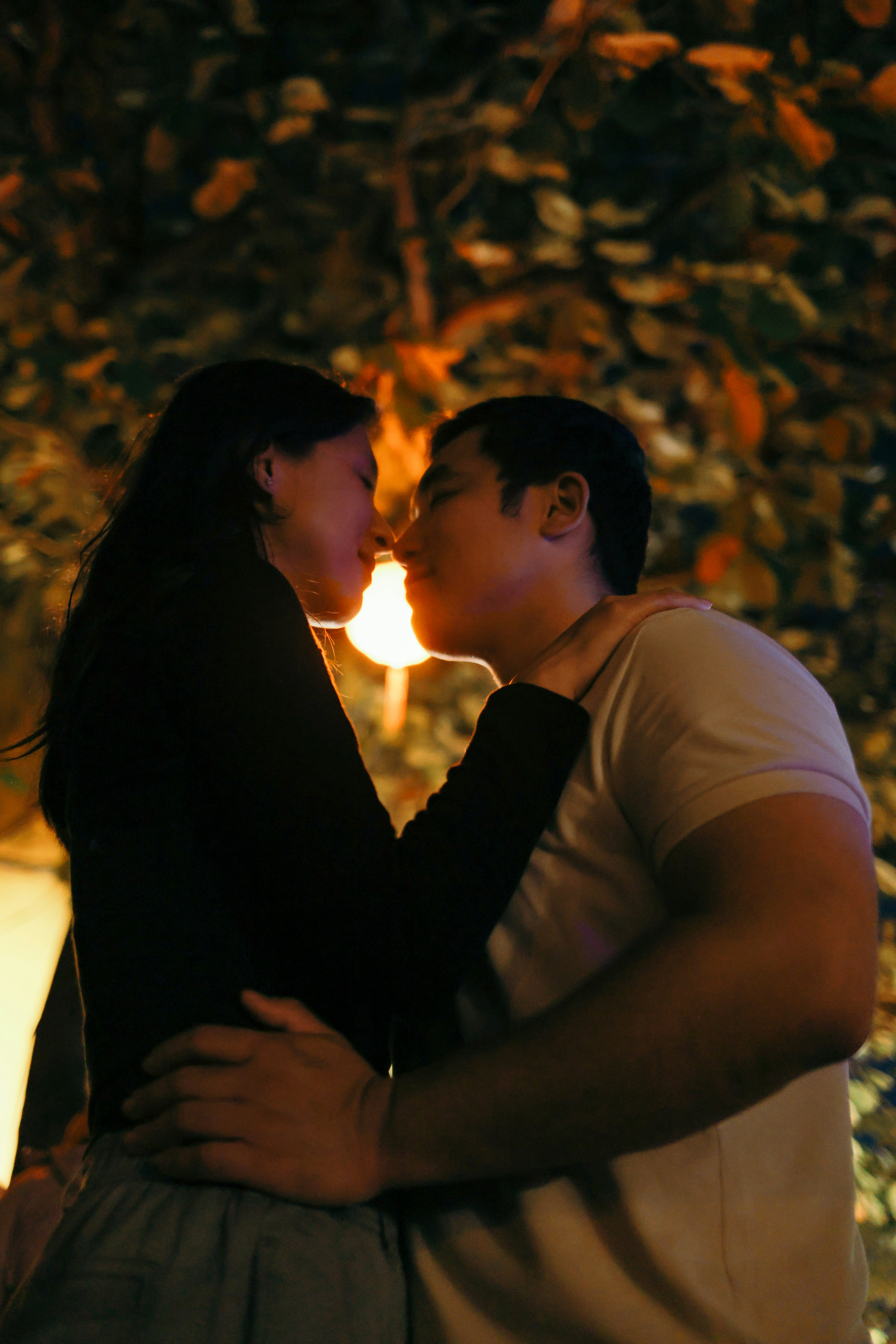 A couple embracing under warm outdoor lights.