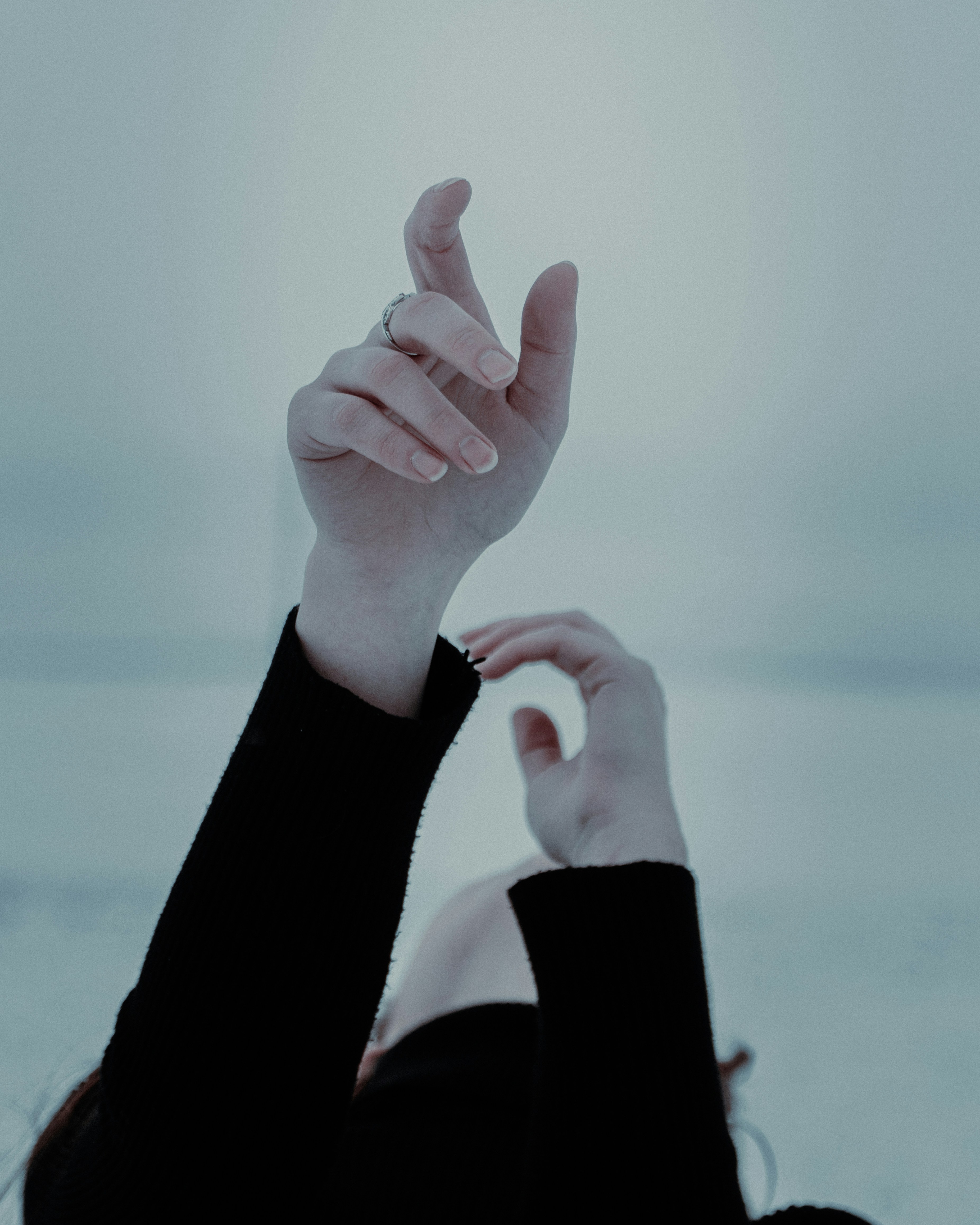 A person's hands reaching up towards a pale sky