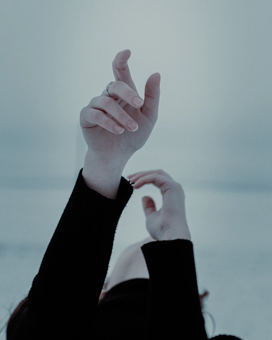 A person's hands reaching up toward a pale, hopeful sky