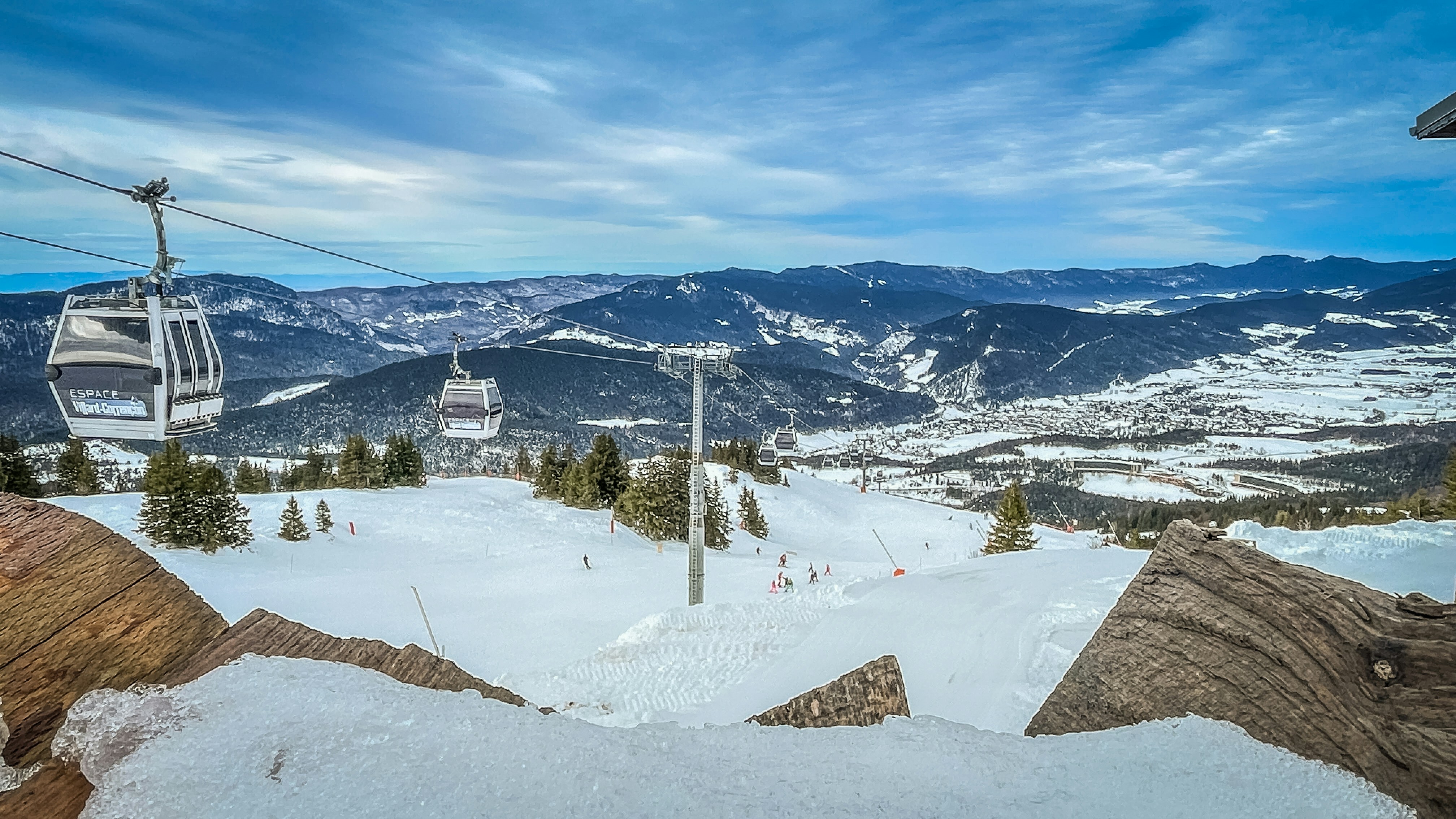 Gondolas ascend a snowy mountain with a village below.