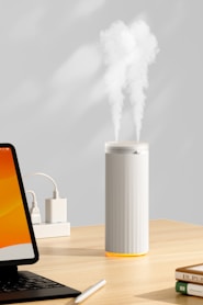 A white humidifier emits mist on a wooden desk.