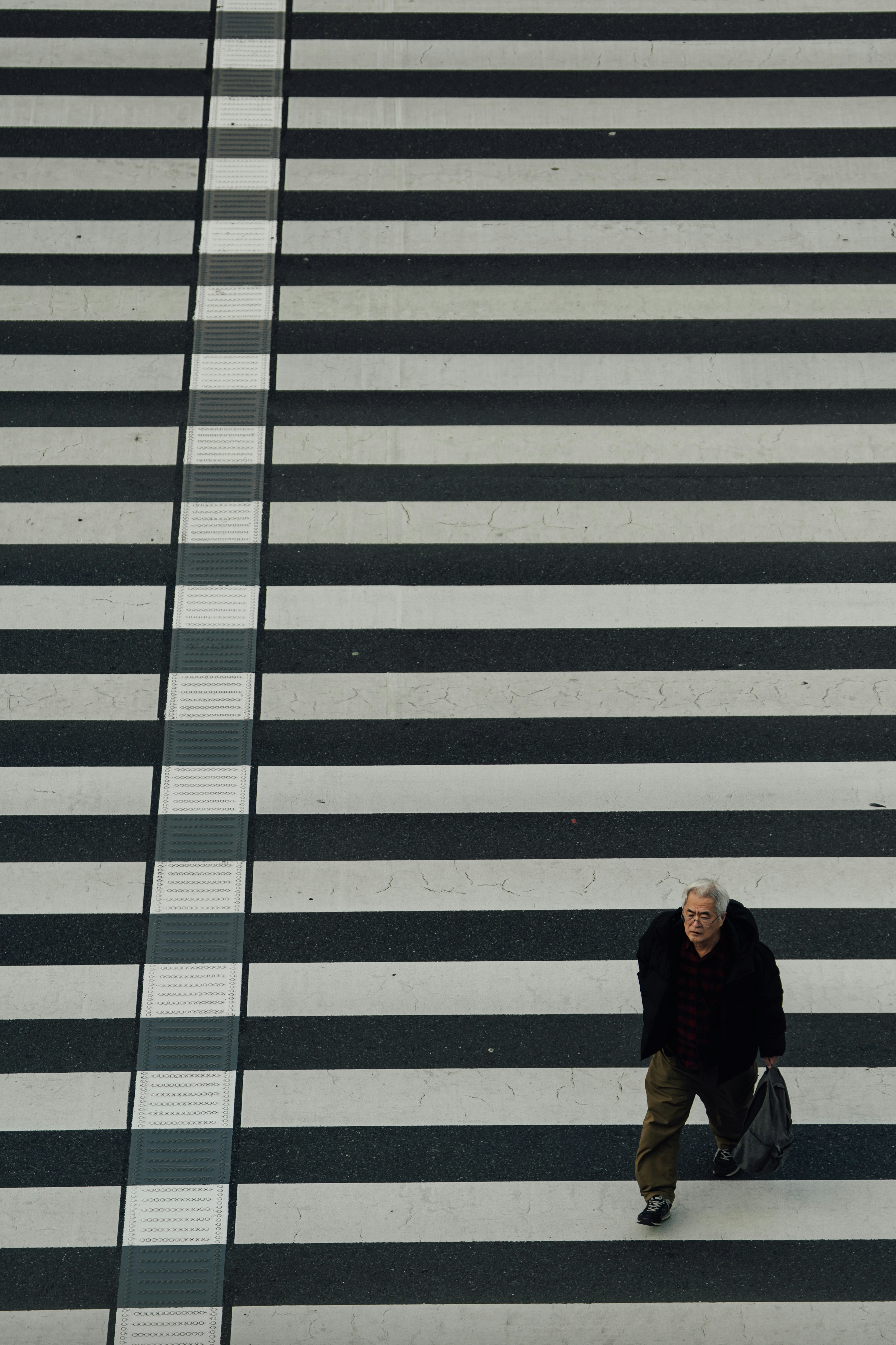 Elderly man walks across a zebra crossing.
