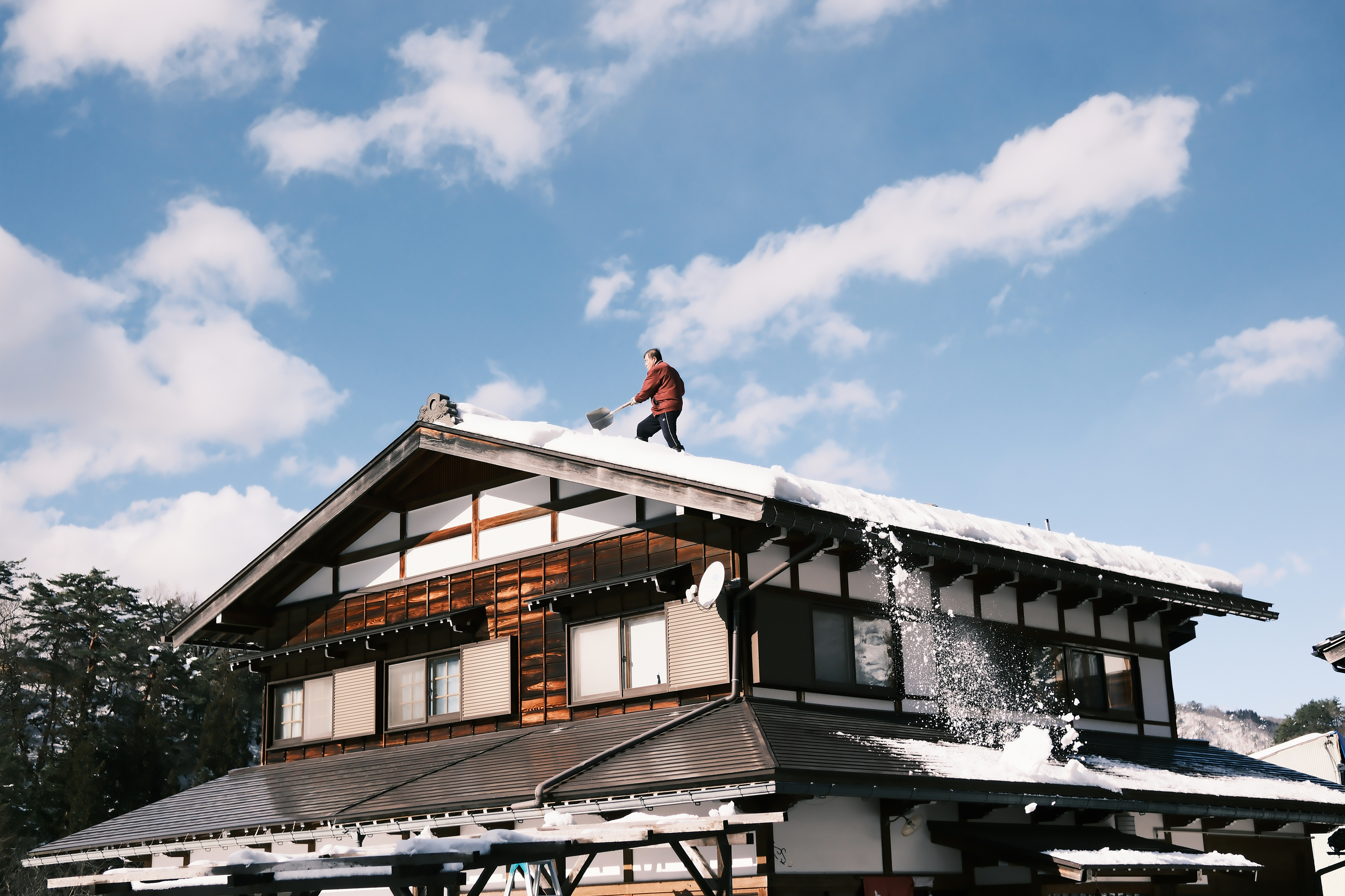 Person clearing snow from a traditional japanese house roof.