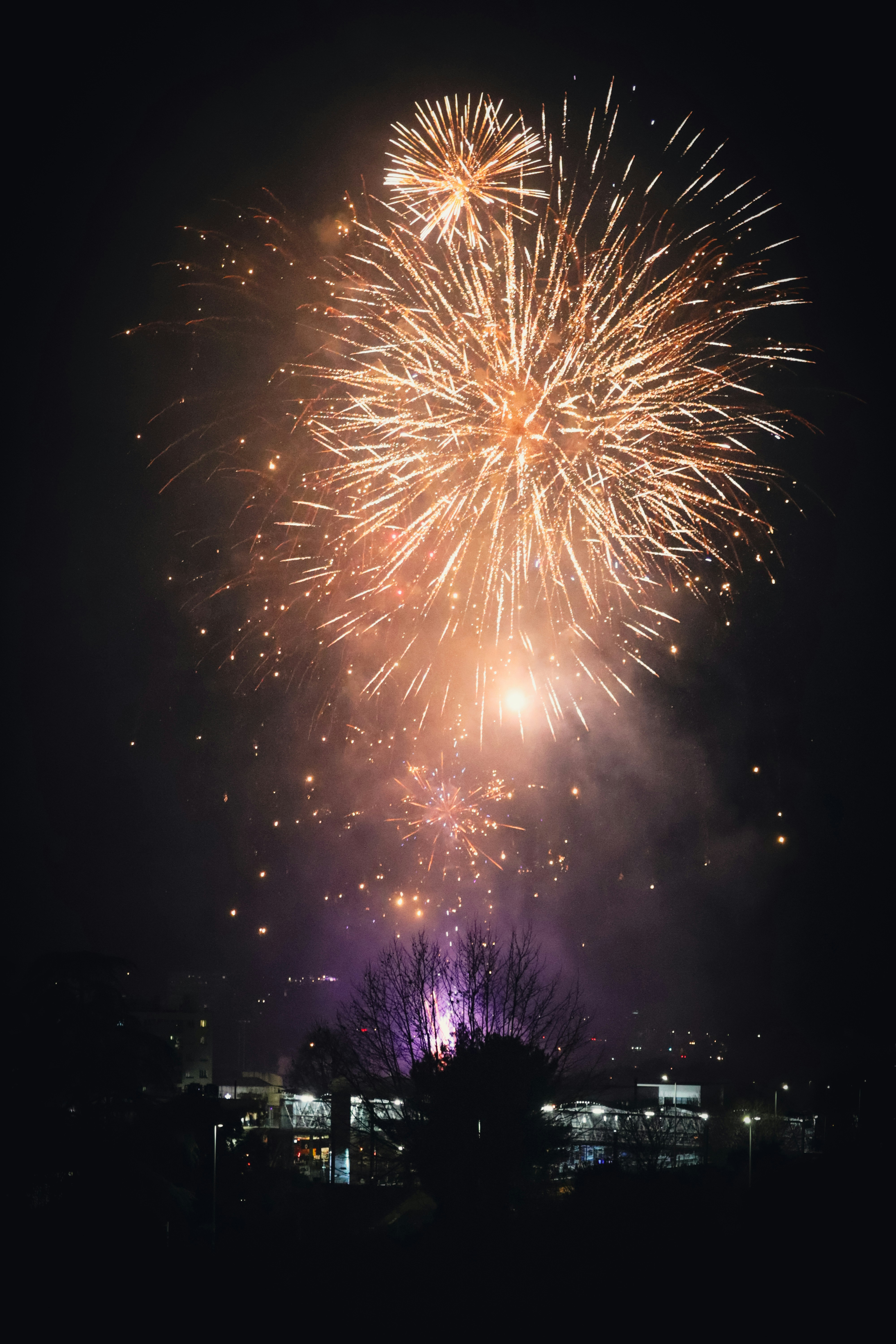 Bright fireworks explode in the night sky above a town.