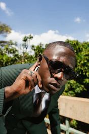 A man in a suit and sunglasses adjusts his earring.