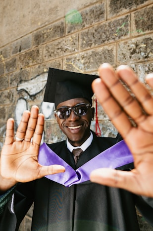 A smiling graduate in cap and gown holds hands up.