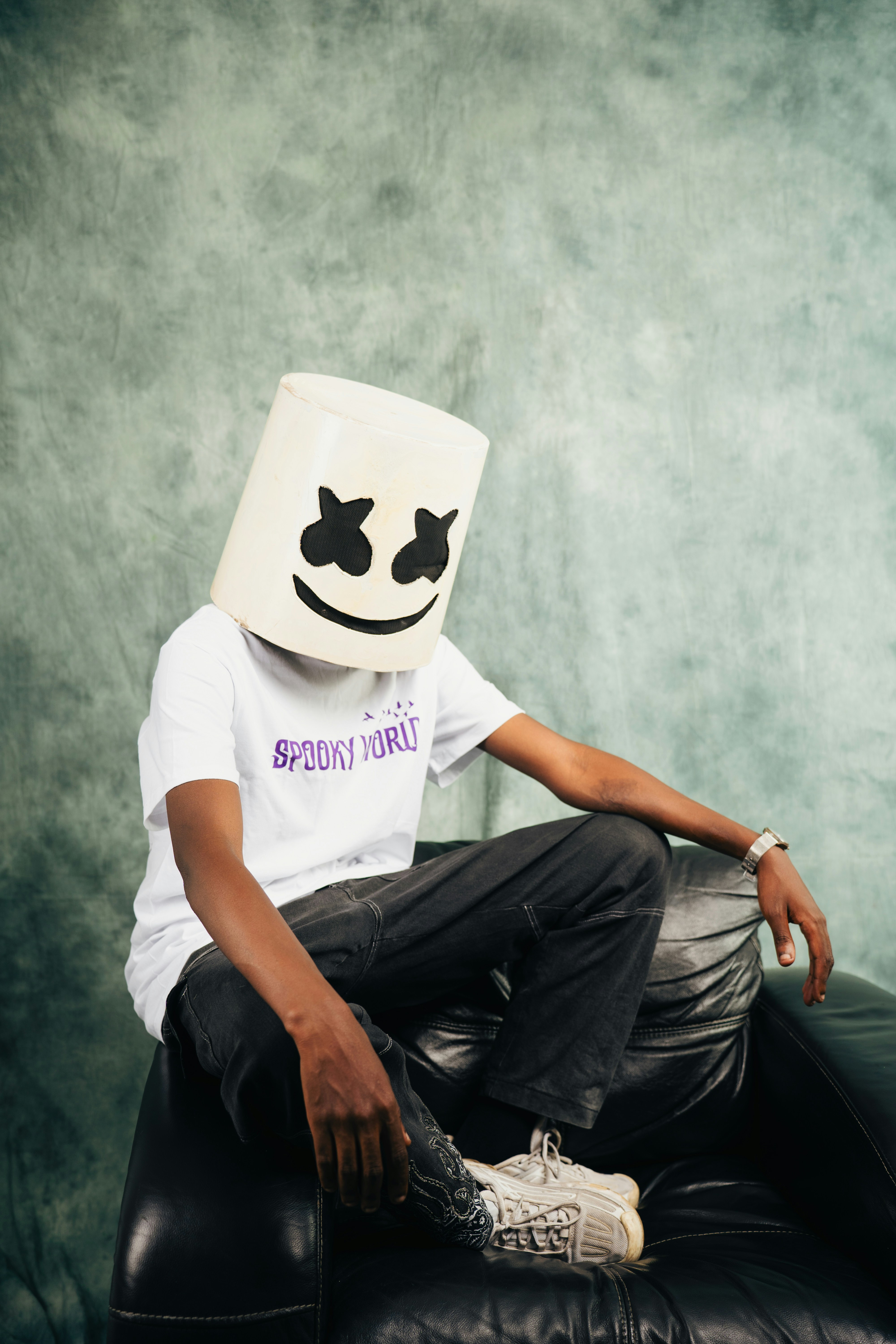 Young person wearing a marshmello mask sits on a couch.