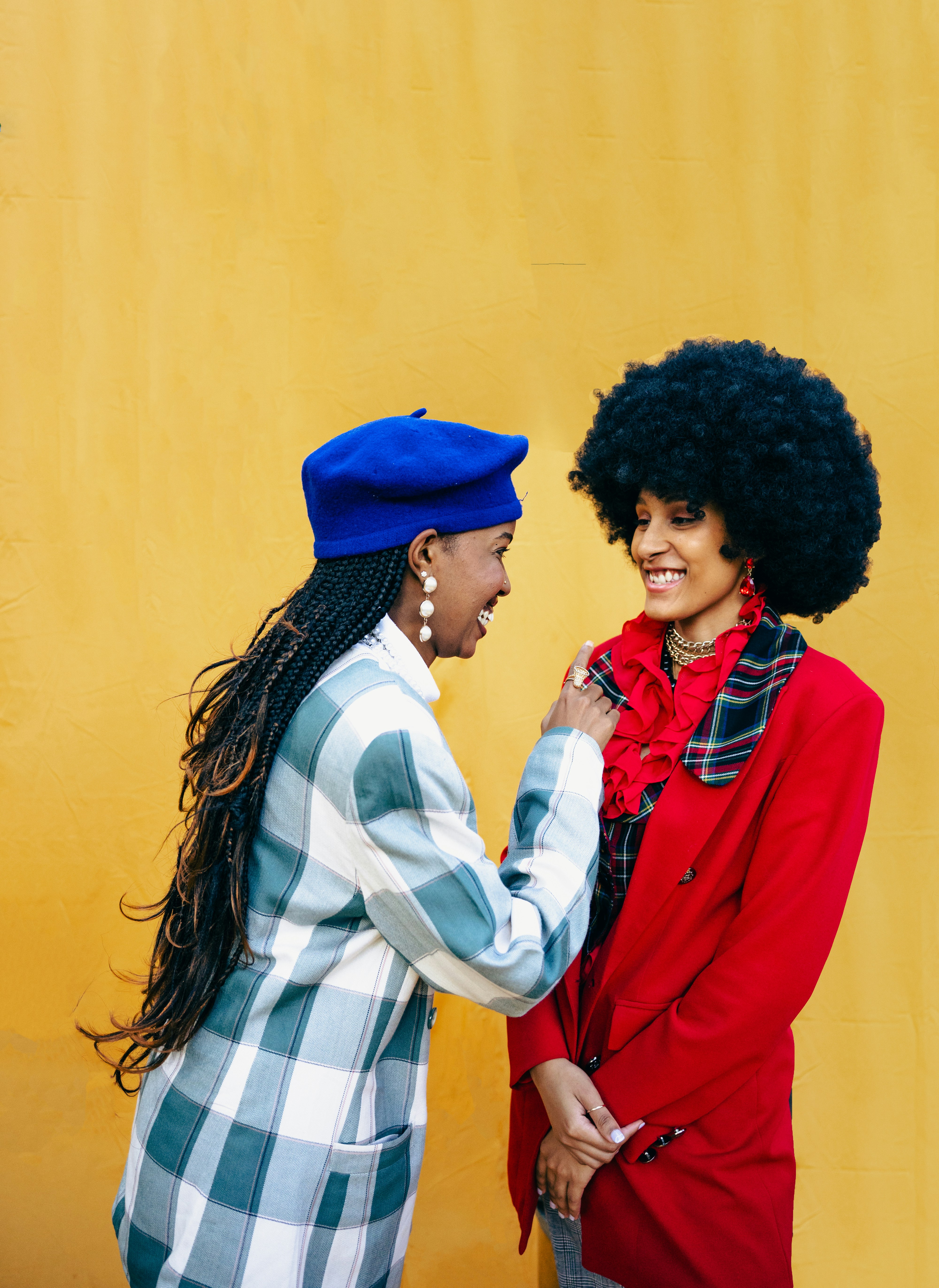 Two stylish women smiling against a yellow wall