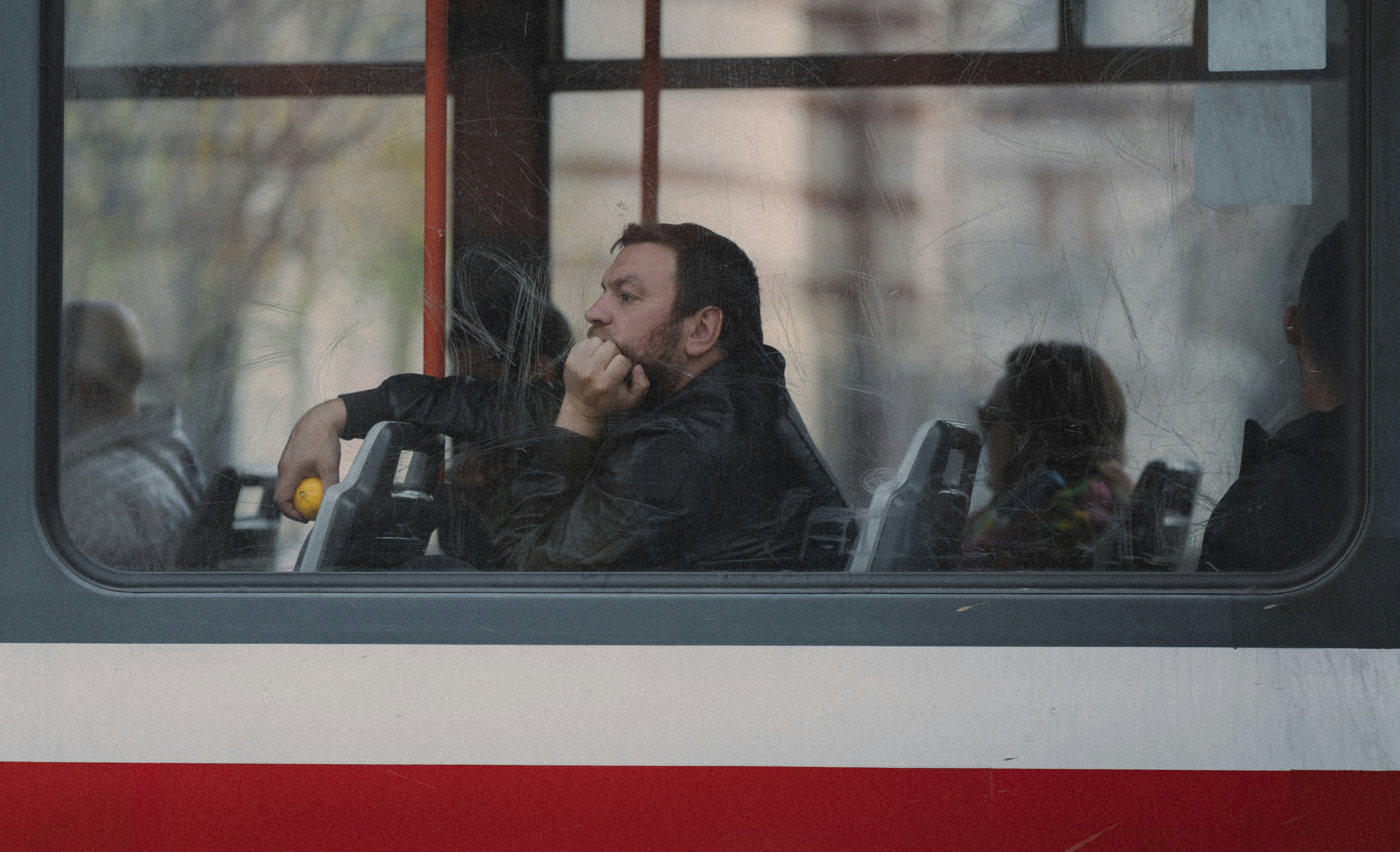 Man looking out bus window with hand on chin.