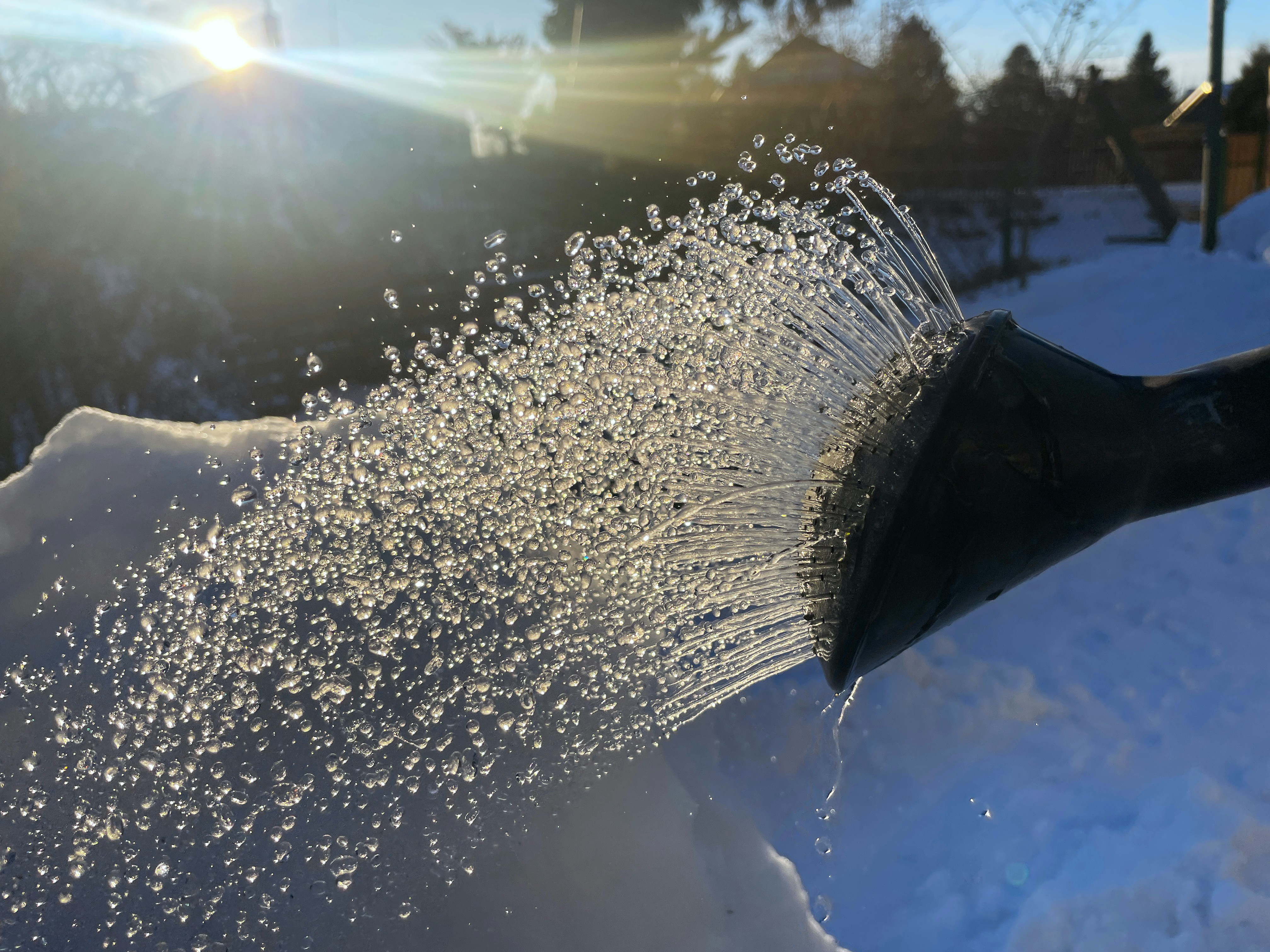Water spraying from a watering can onto snow.