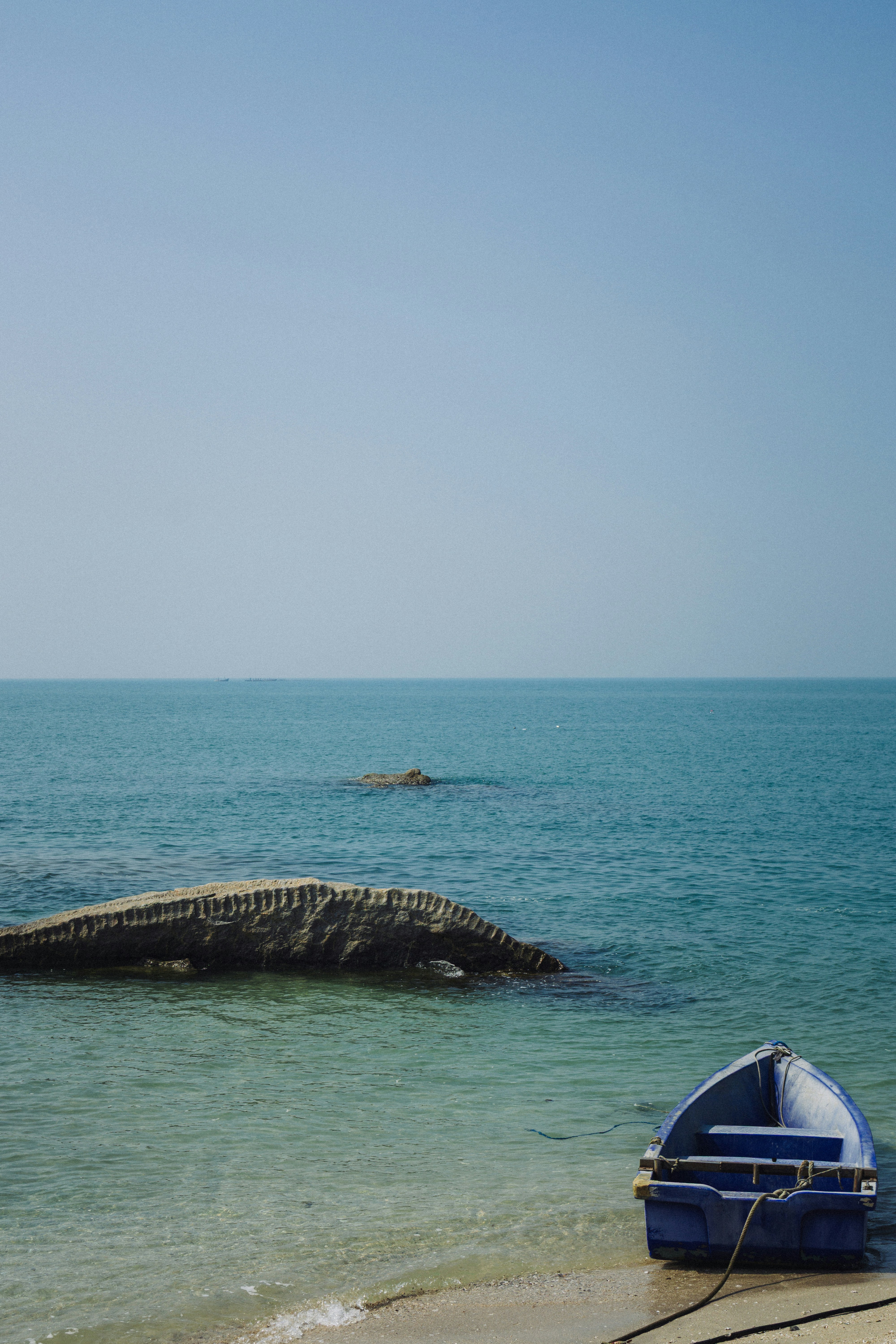 A blue boat rests on a sandy shore beside rocks.