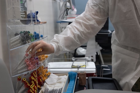 Person in lab coat selecting supplies from rack.