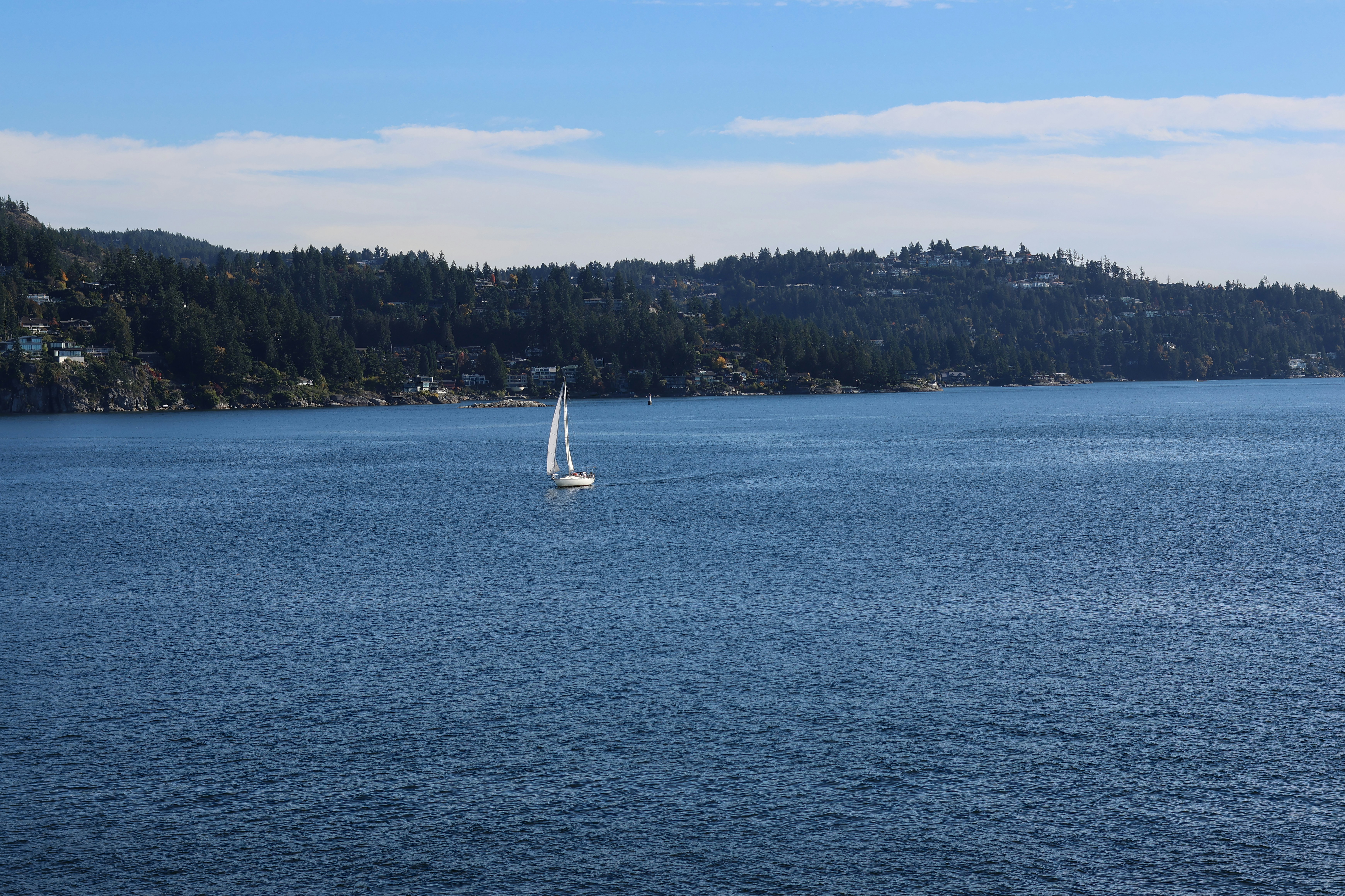 A lone sailboat glides across a calm blue sea.