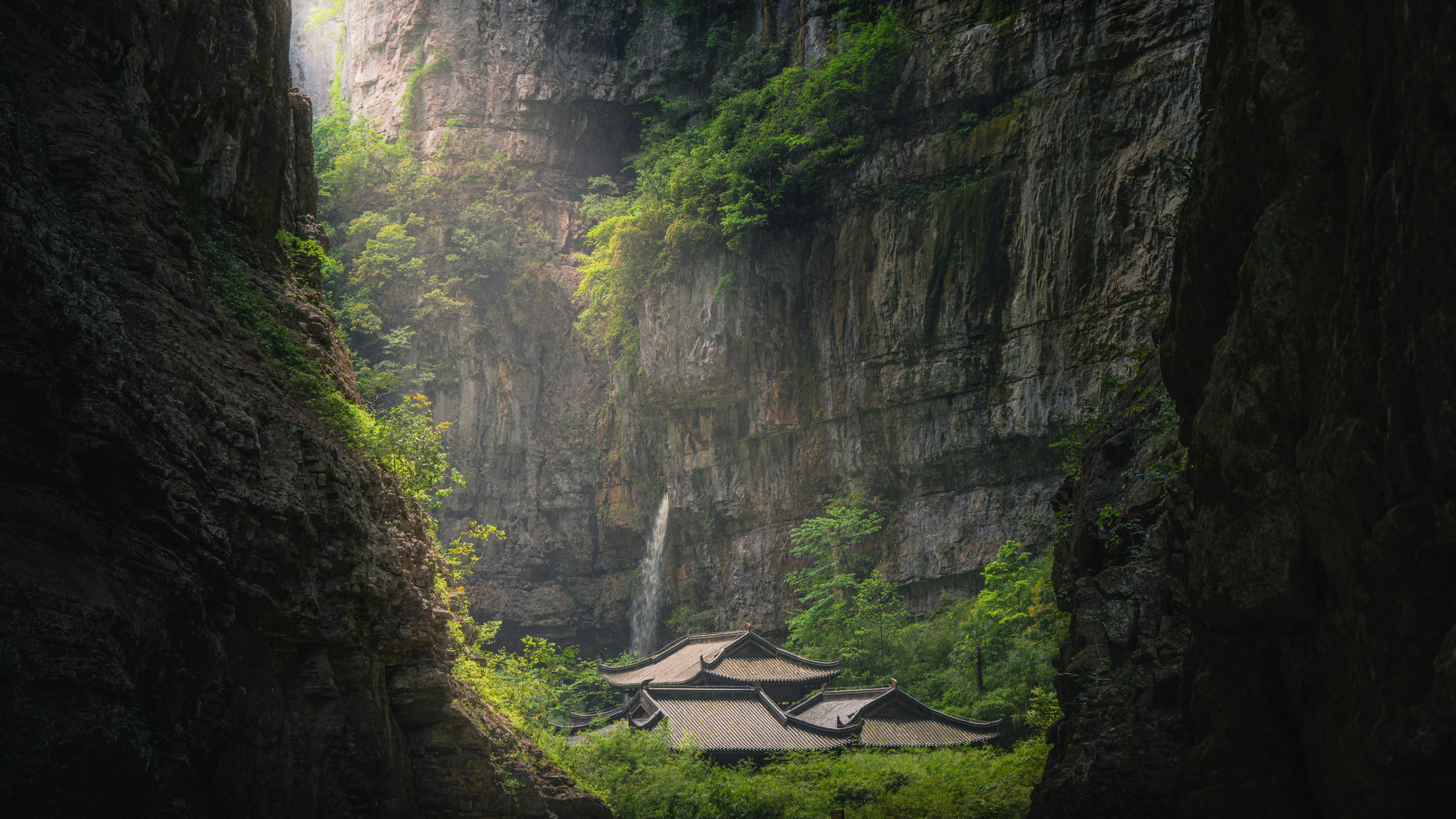 Waterfall cascades into a hidden valley with ancient buildings.