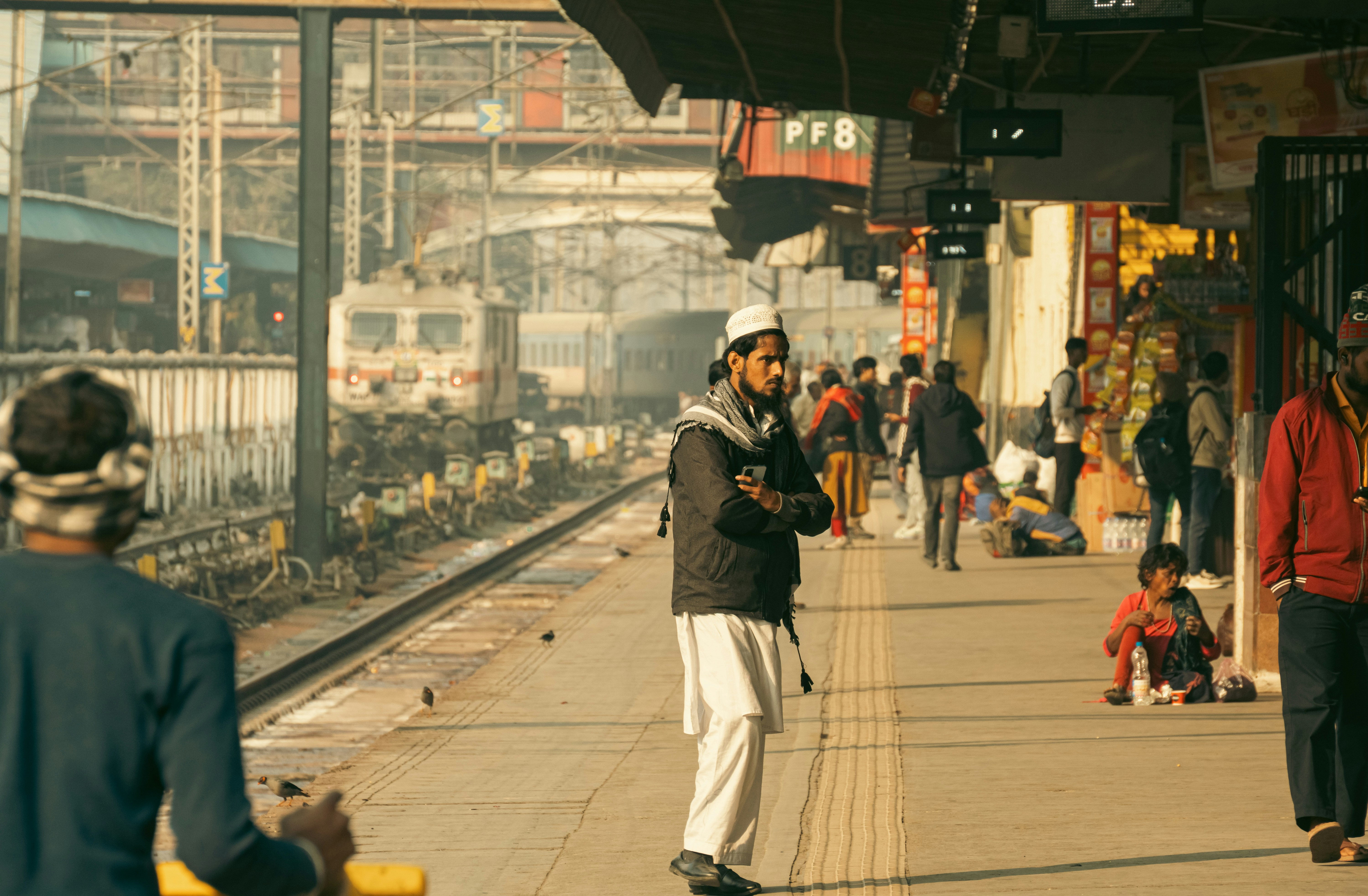 Busy New Delhi Railway Station platform with a train arriving, passengers disembarking and looking for transport options.