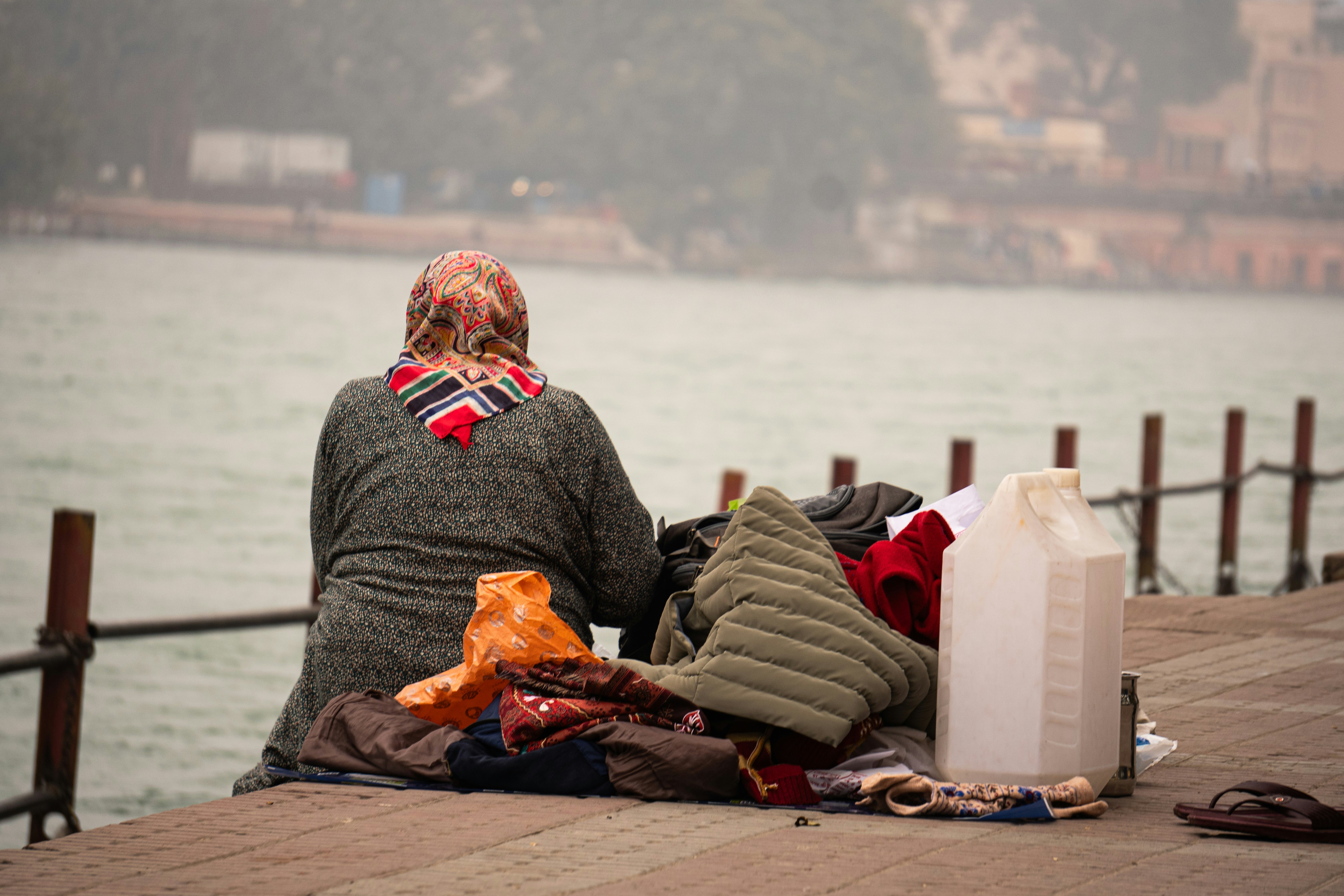 Persona sentada junto al agua con pertenencias