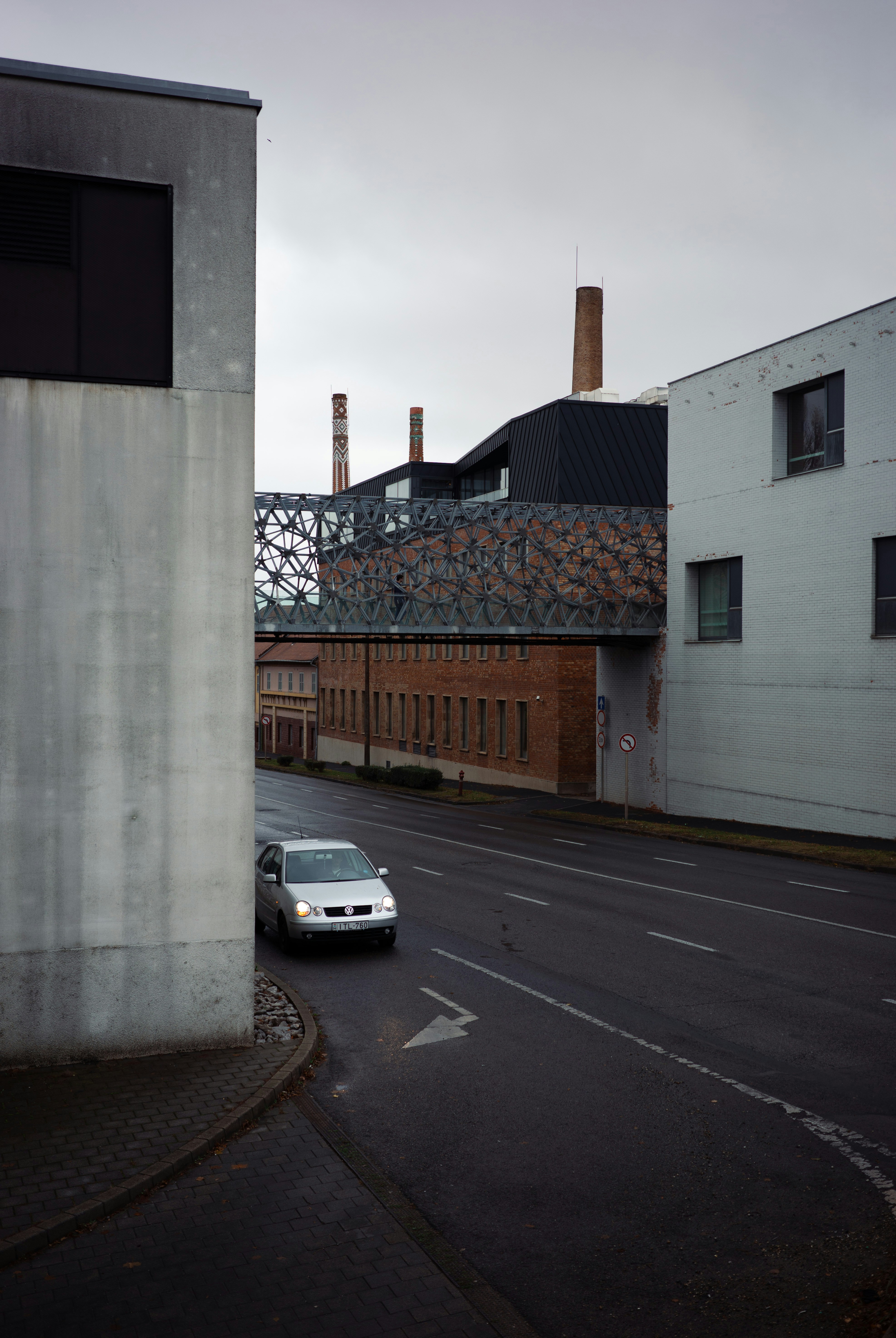Silver car drives on wet road between buildings.