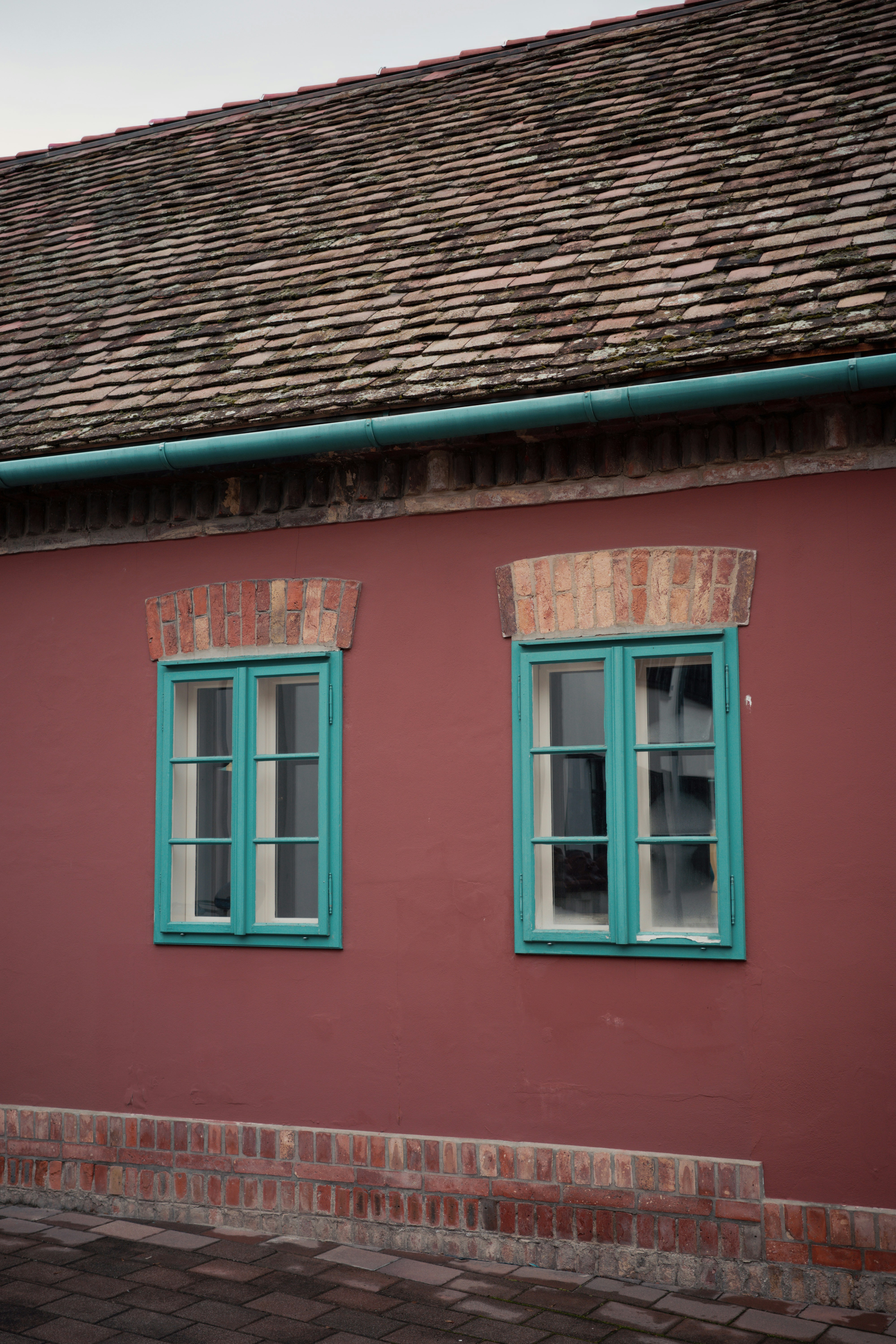 Red wall with two teal windows and tiled roof
