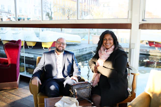Two people sitting by a window with boats outside