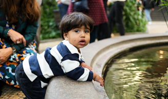 A young child leans over a fountain's edge.