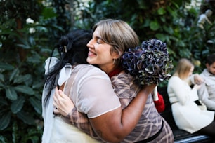 Two women embracing, one holding a bouquet.