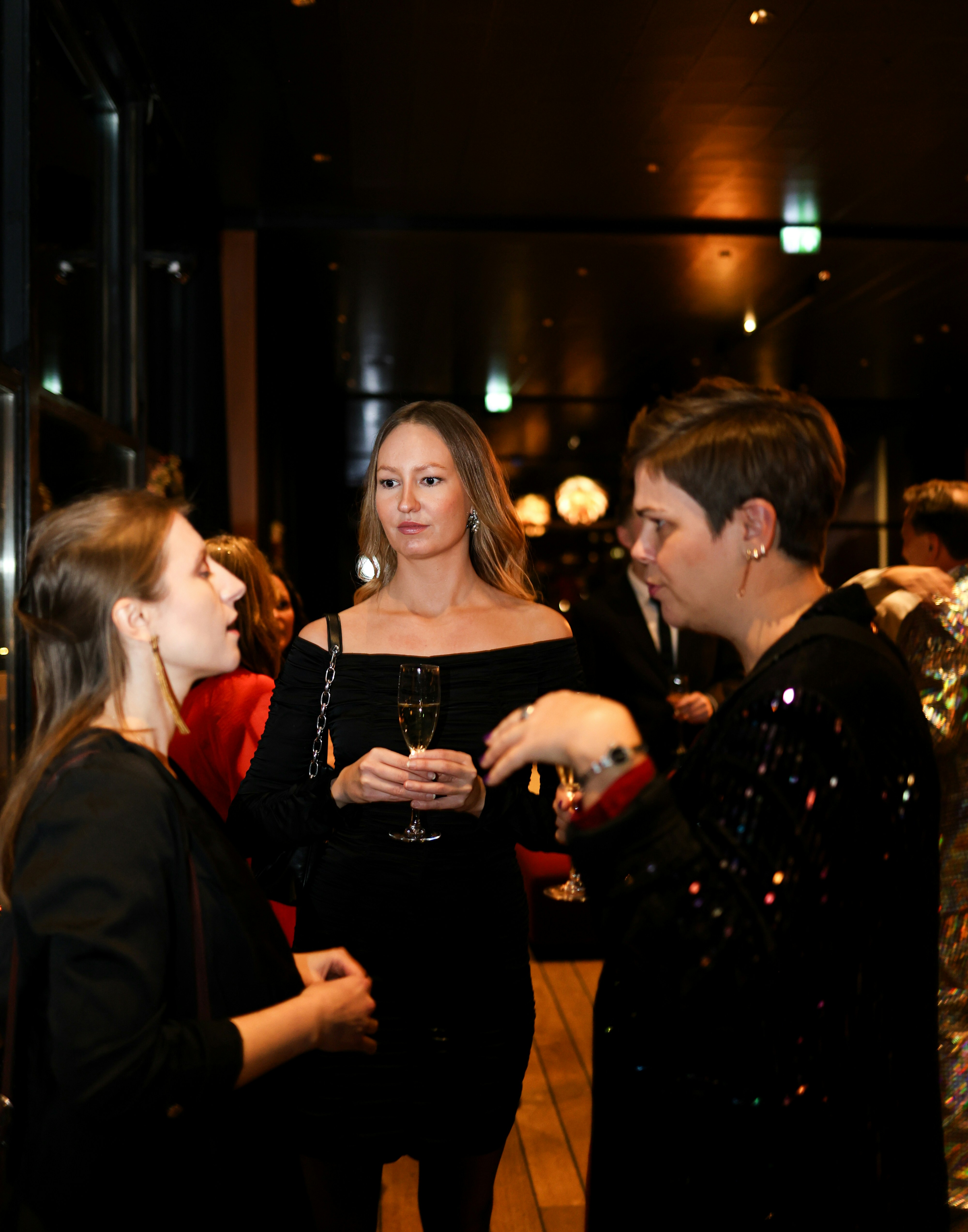 Three women in formal attire talking at an event
