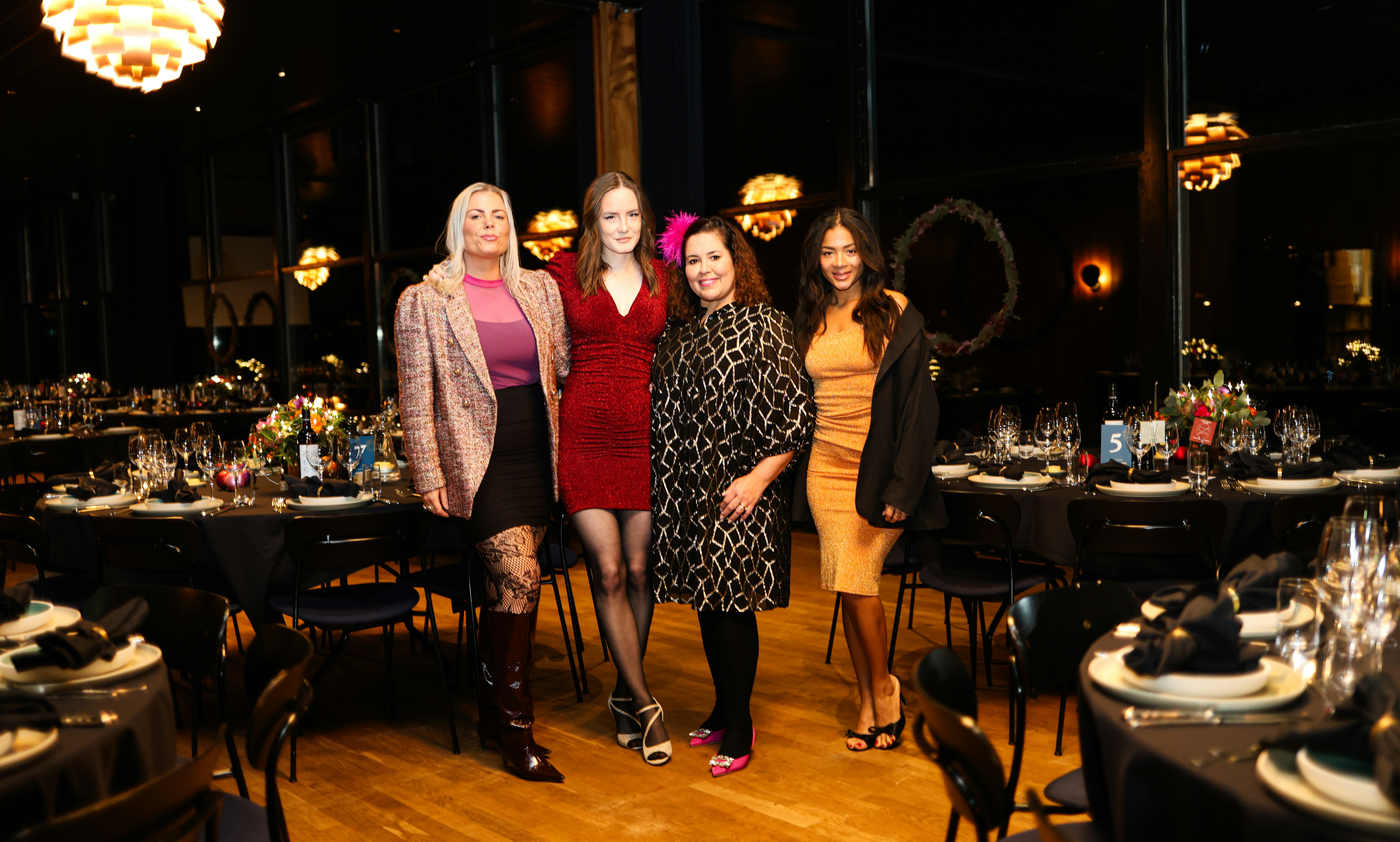 Four women pose in a dimly lit event space.