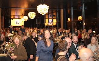 A woman smiles at a formal gathering with many people