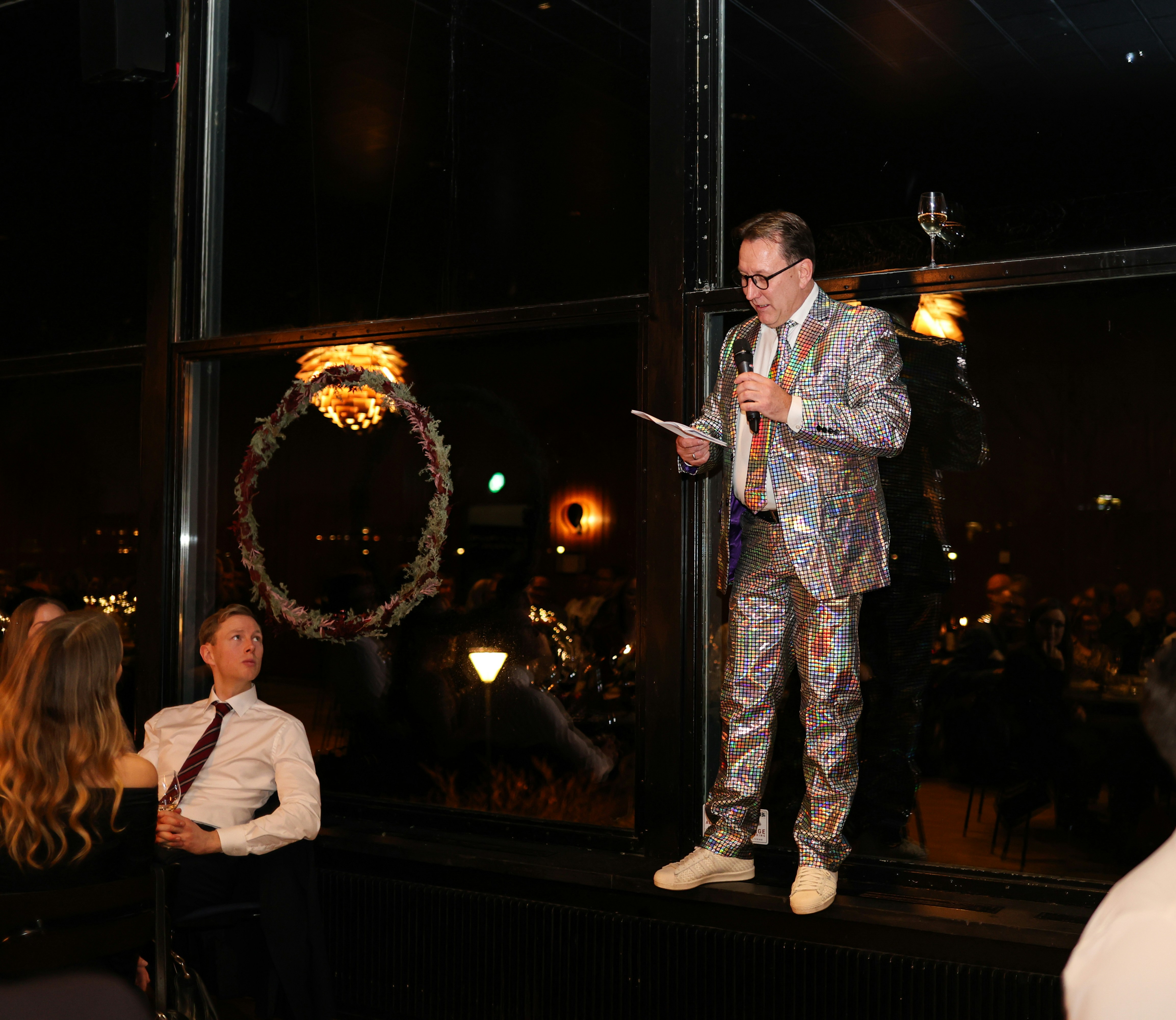 Man in sparkly suit speaks at event near window