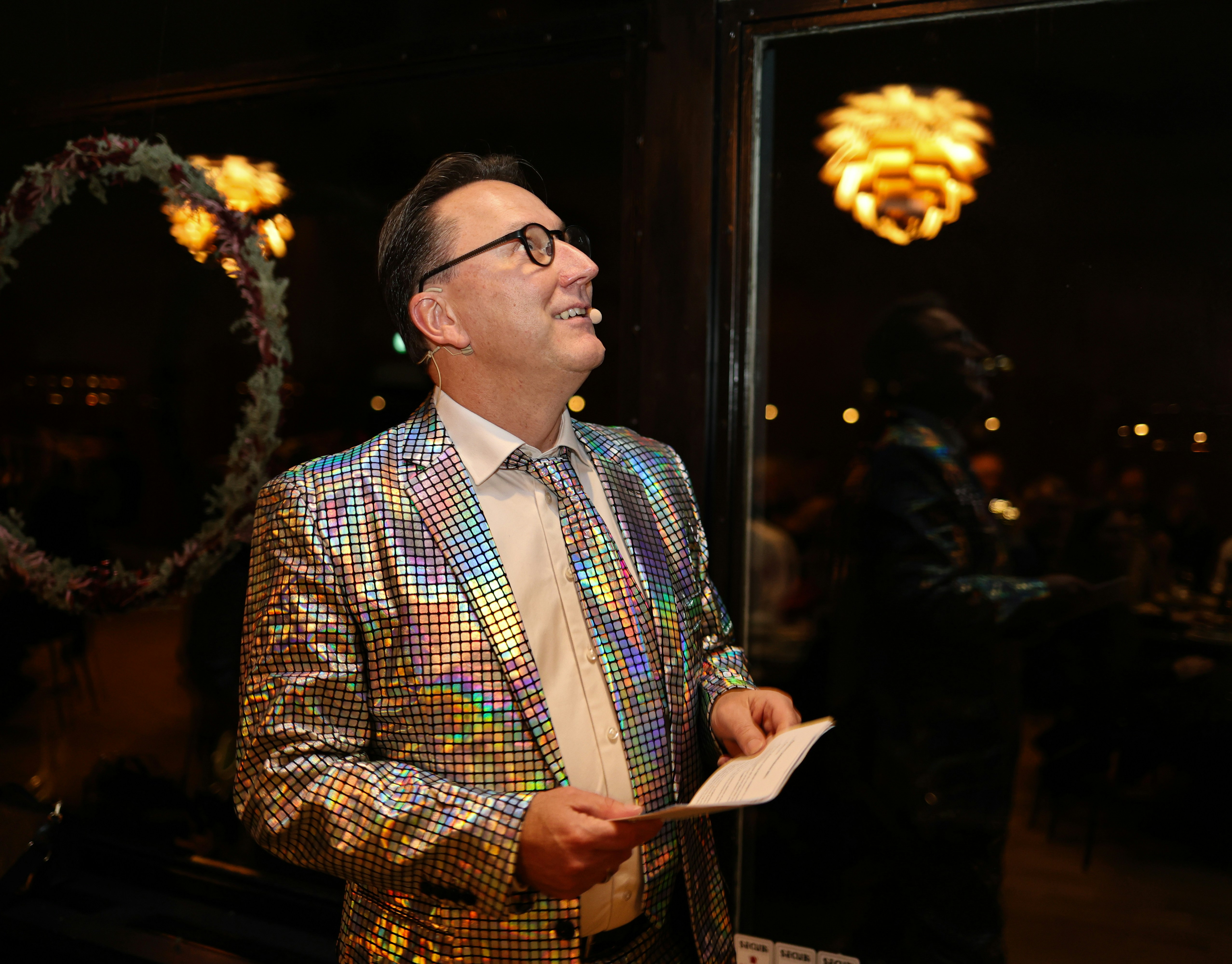 Man in sparkly jacket holding paper indoors paper, looking up