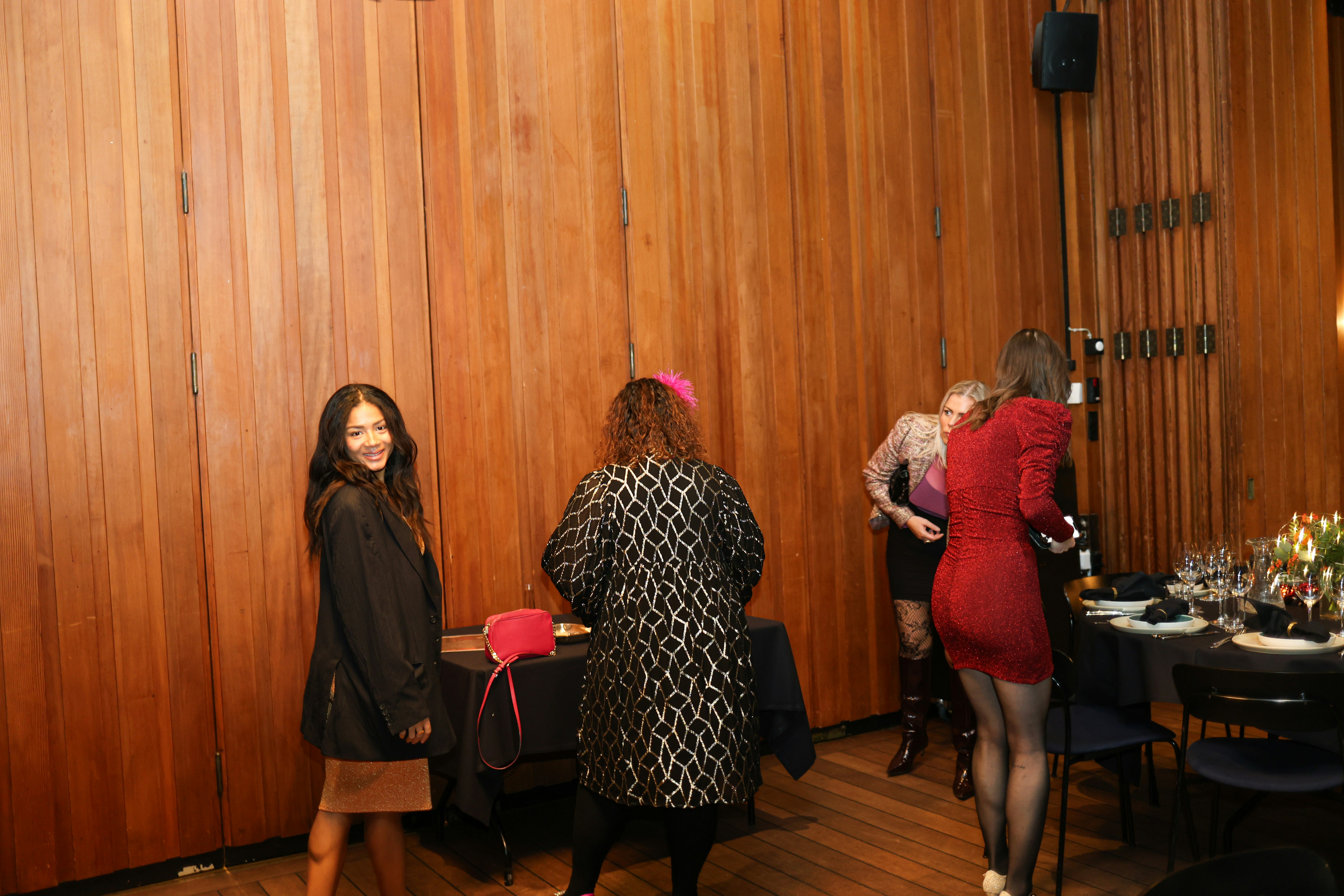 Four women in formal attire socialize at a dining table.
