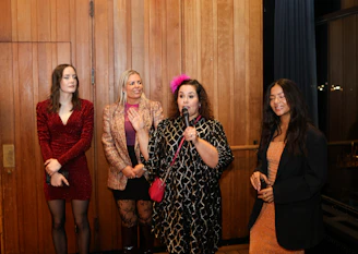 Four women stand together, one speaking into a microphone.