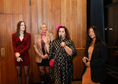 Four women stand together, one speaking into a microphone.