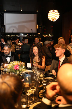 People seated at a formal dinner with floral centerpieces.