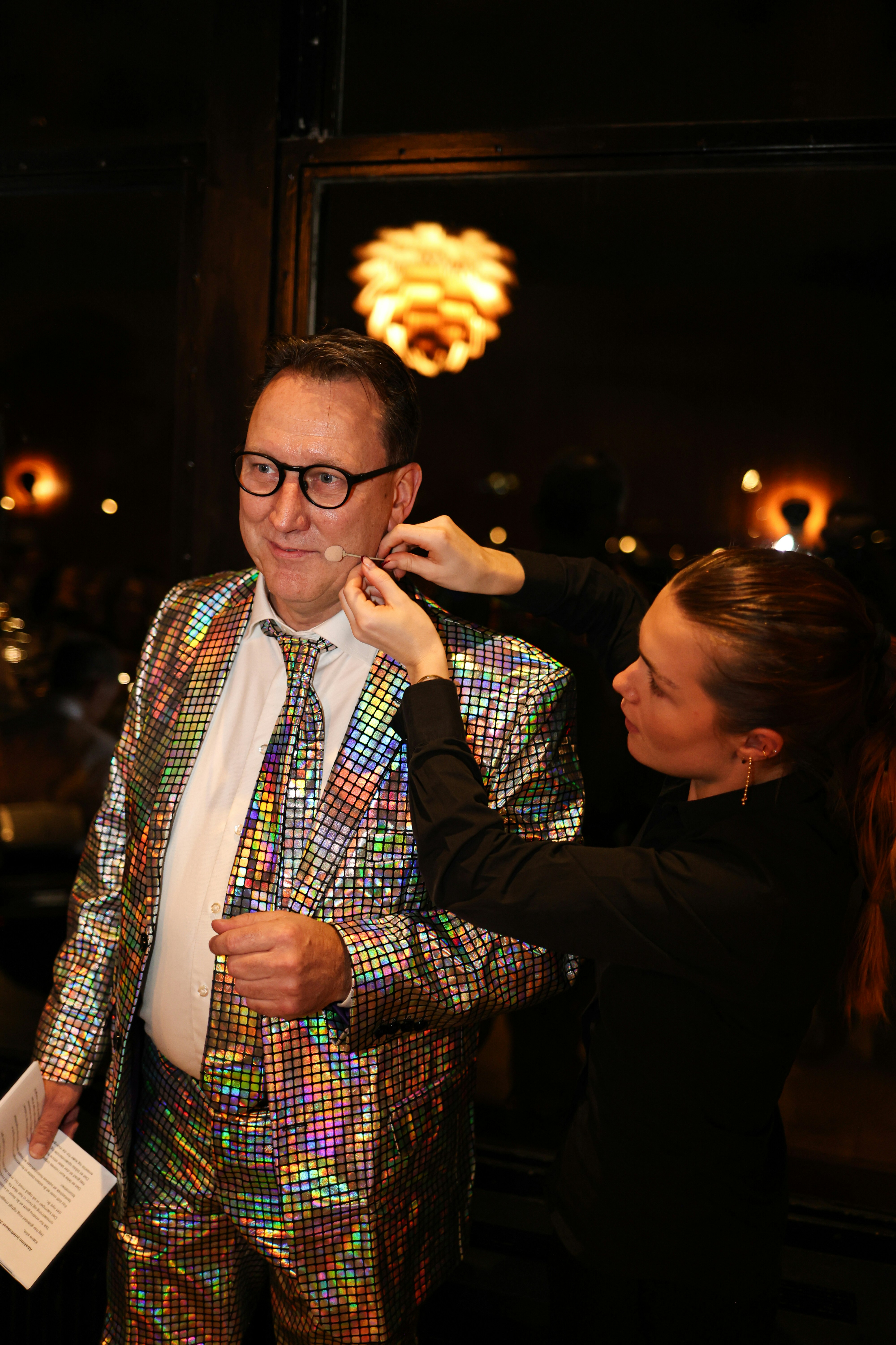 A man in a sparkly suit gets his tie adjusted