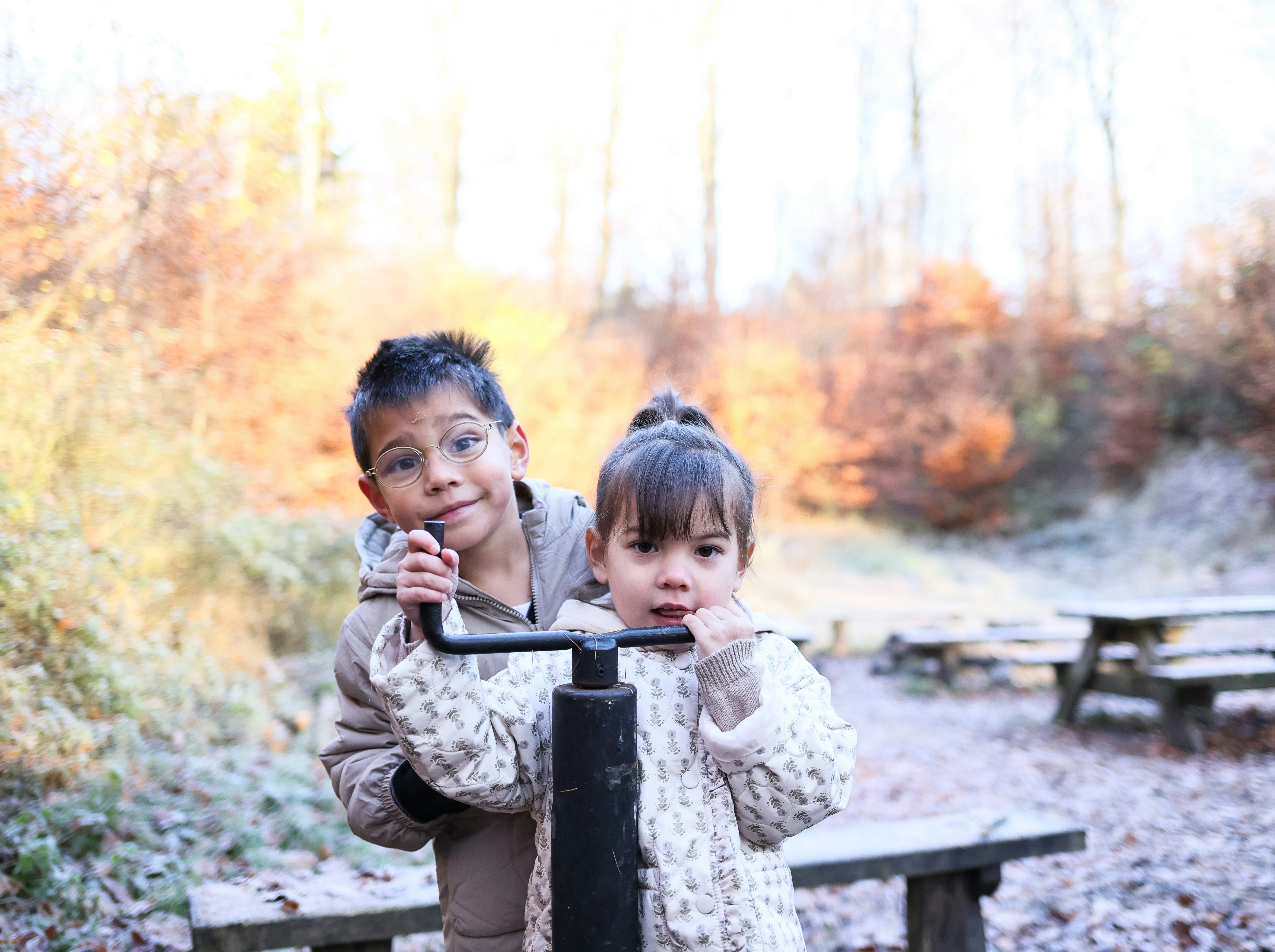 Dos niños están junto a una barra metálica al aire libre.